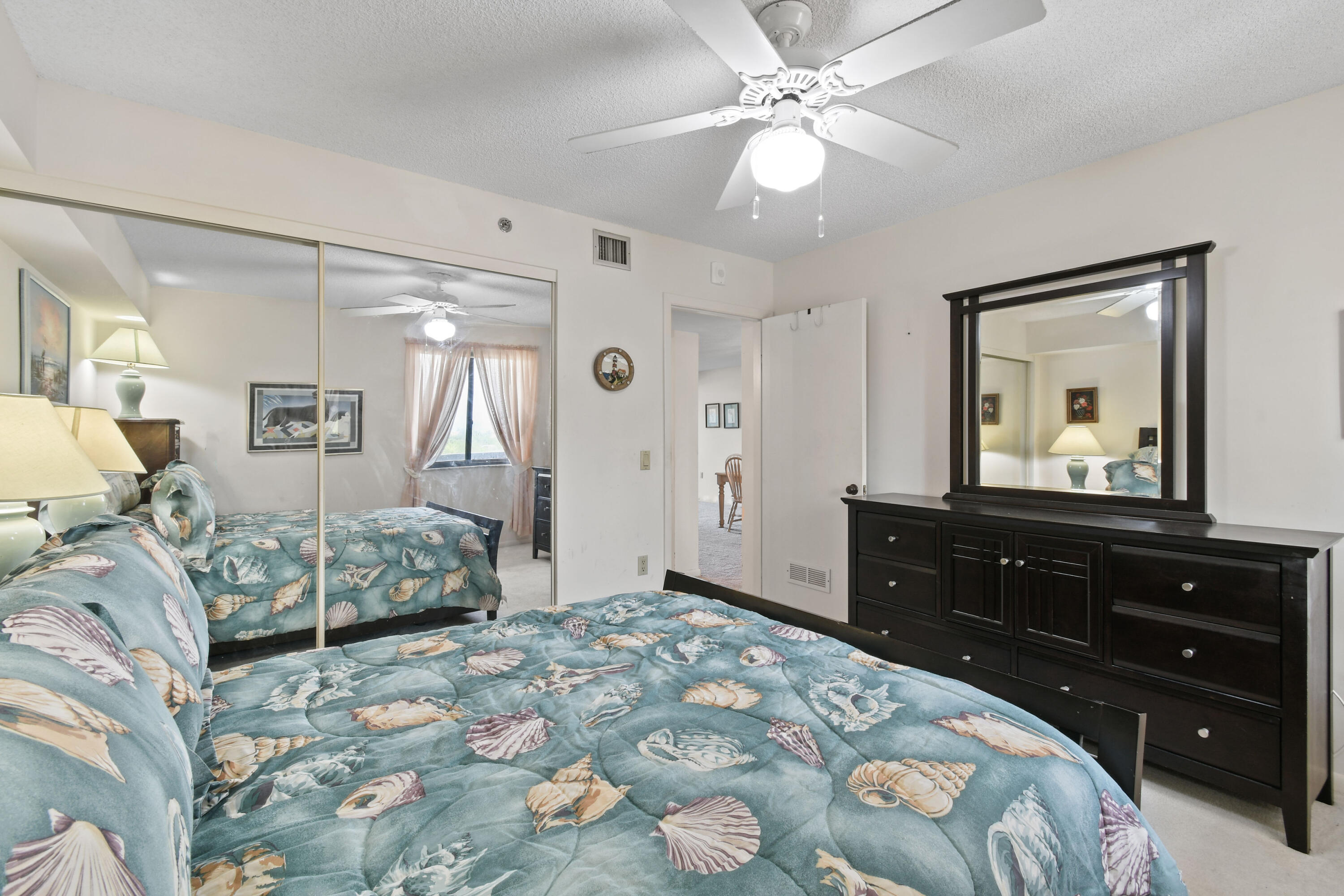 Furnished bedroom with a blue seashell-patterned bedspread and dark wood dresser with mirror.