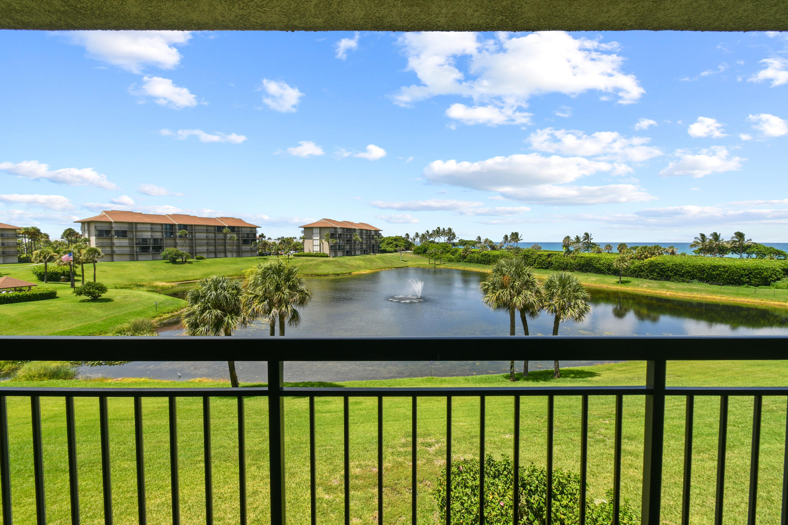 Balcony view over a fountain pond, landscaped grounds, neighboring condos, and the ocean.