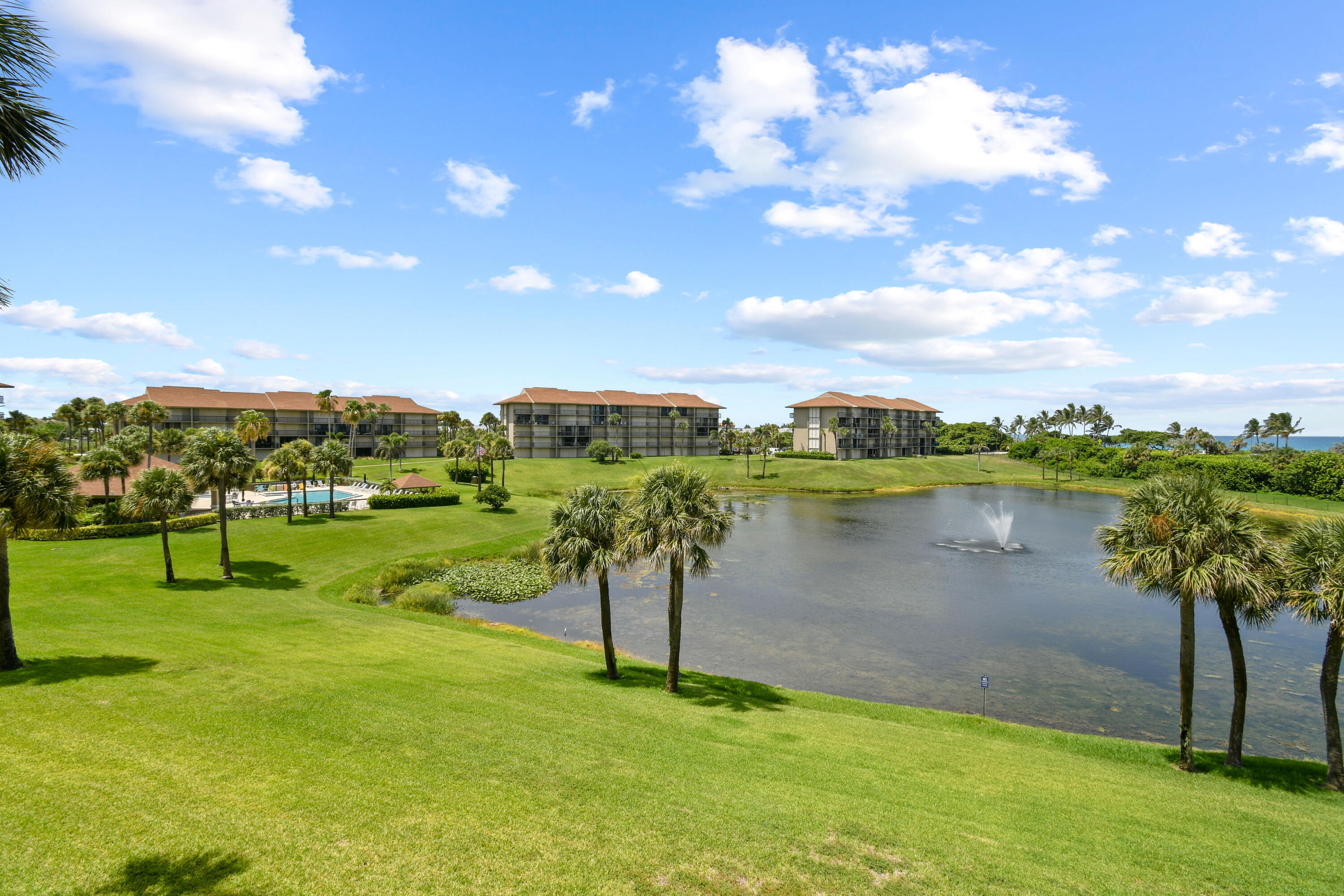 Condominium grounds with palm trees, a pond fountain, and a glimpse of ocean.