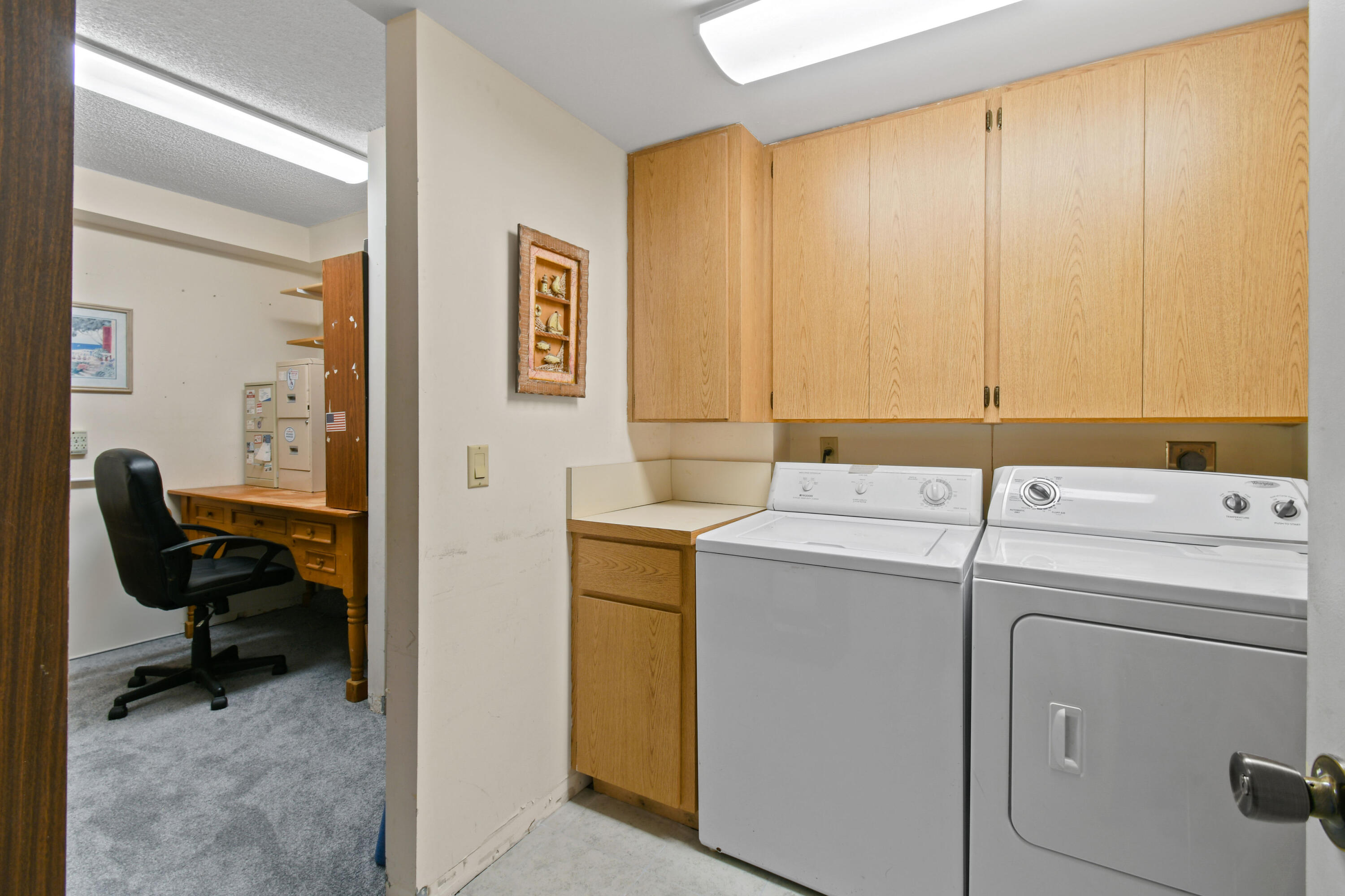 Laundry room with white washer and dryer, light wood cabinets, and an adjoining office nook.