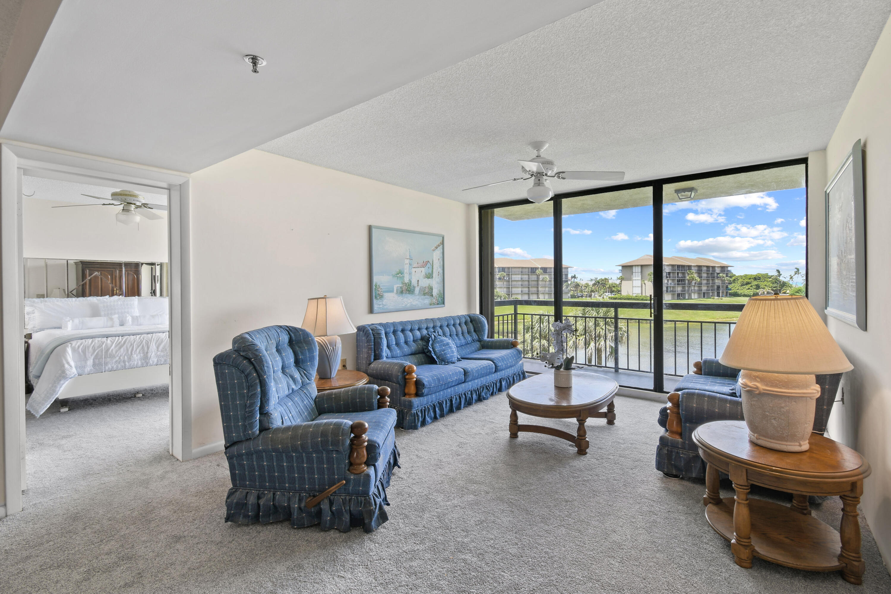 Living room with blue seating and balcony views over water and neighboring buildings.