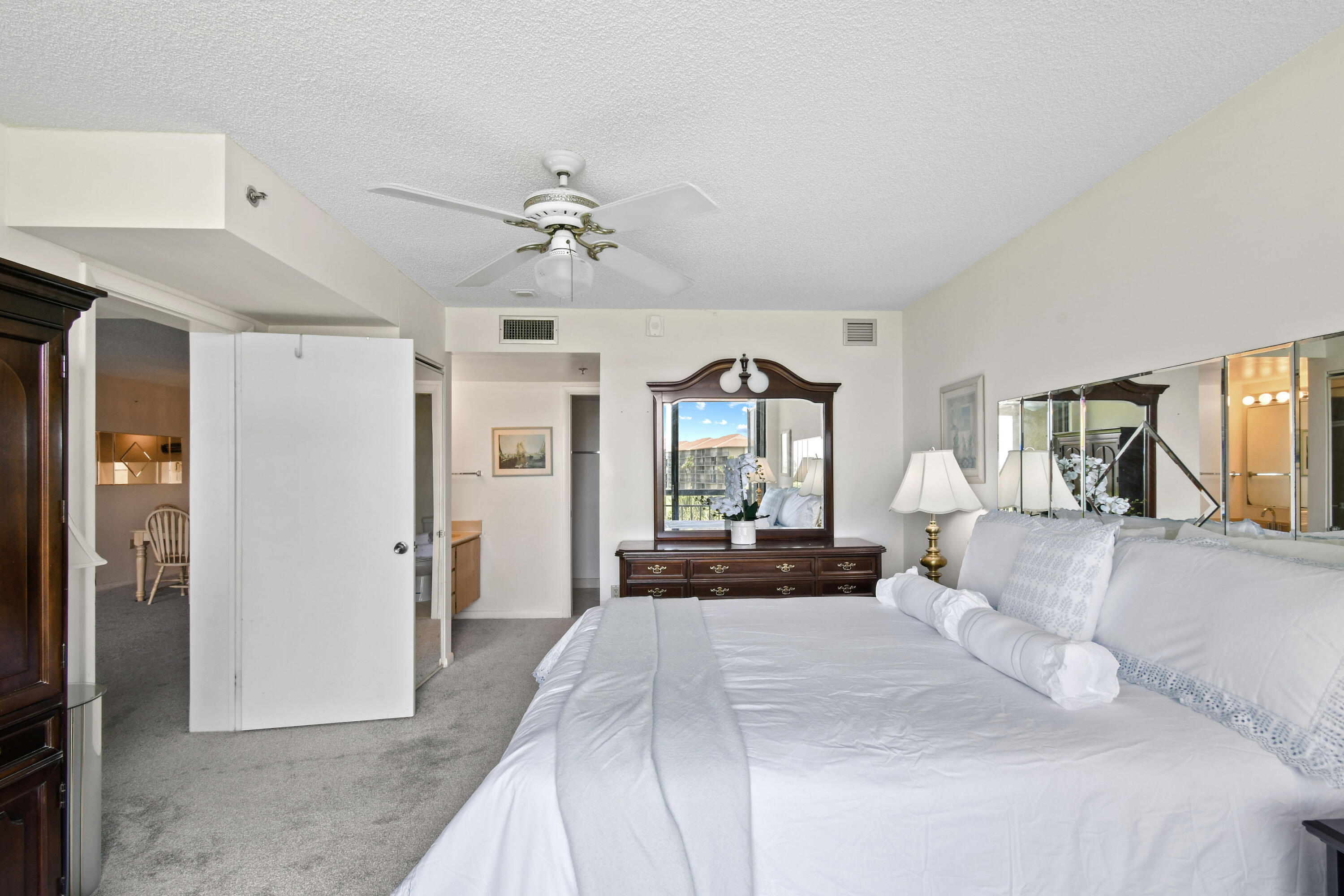 Bedroom with a large white bed, dark wood dresser and mirror, and a window facing a neighboring building.