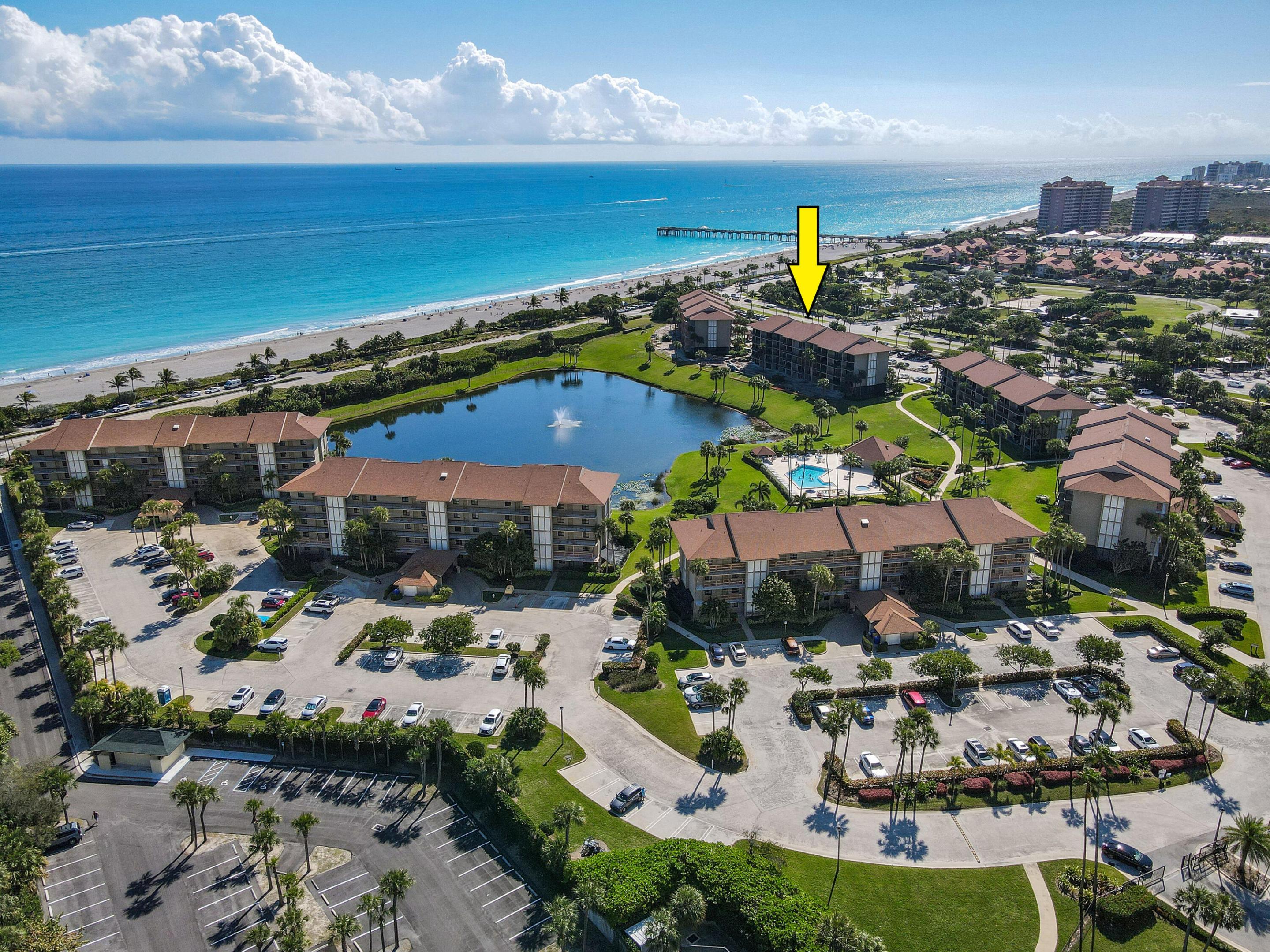 Aerial view of a beachfront condominium complex, with an arrow marking a building beside the pool and lagoon.