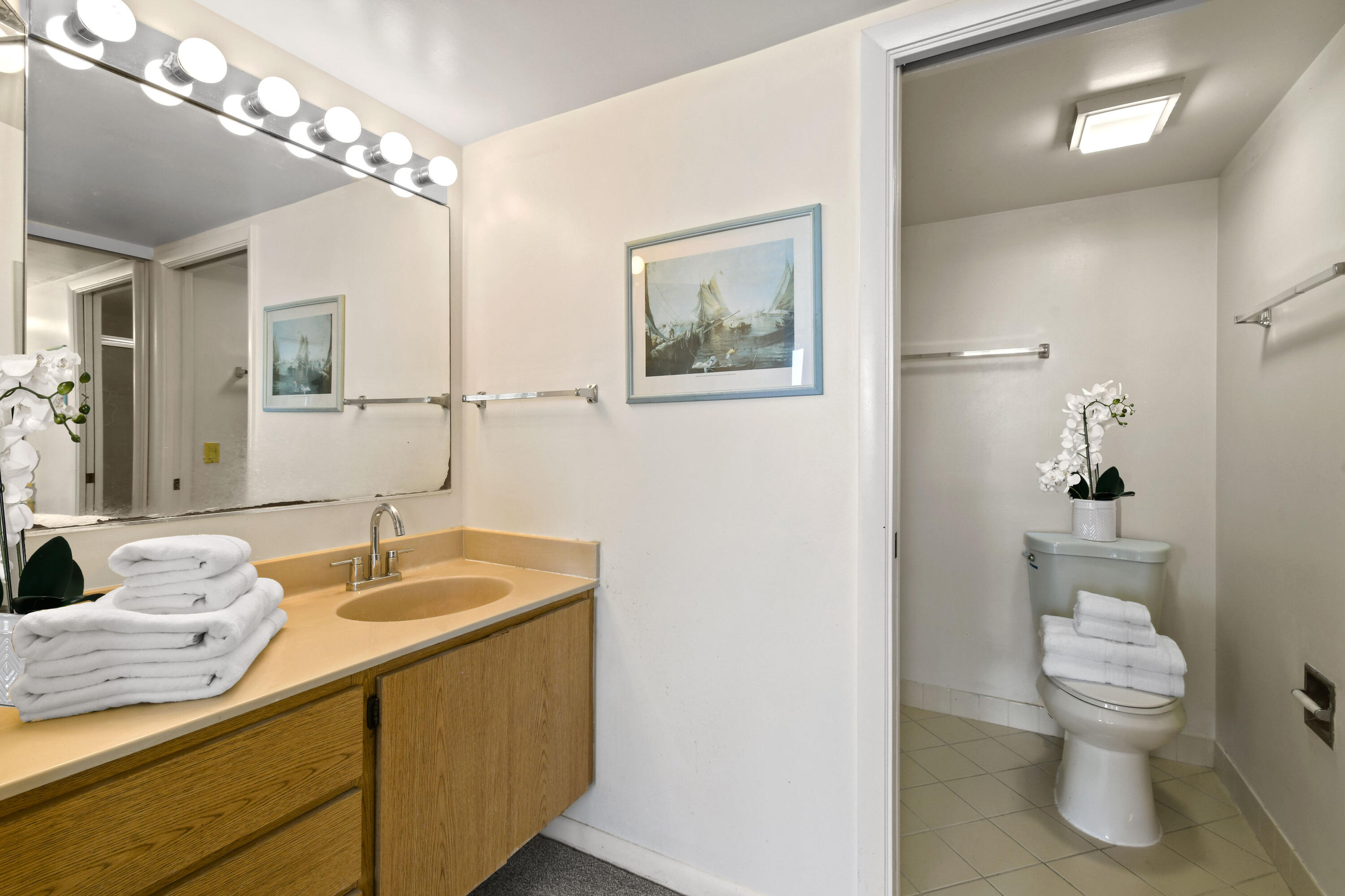 Bathroom with wood vanity and illuminated mirror, opening to a separate toilet area.