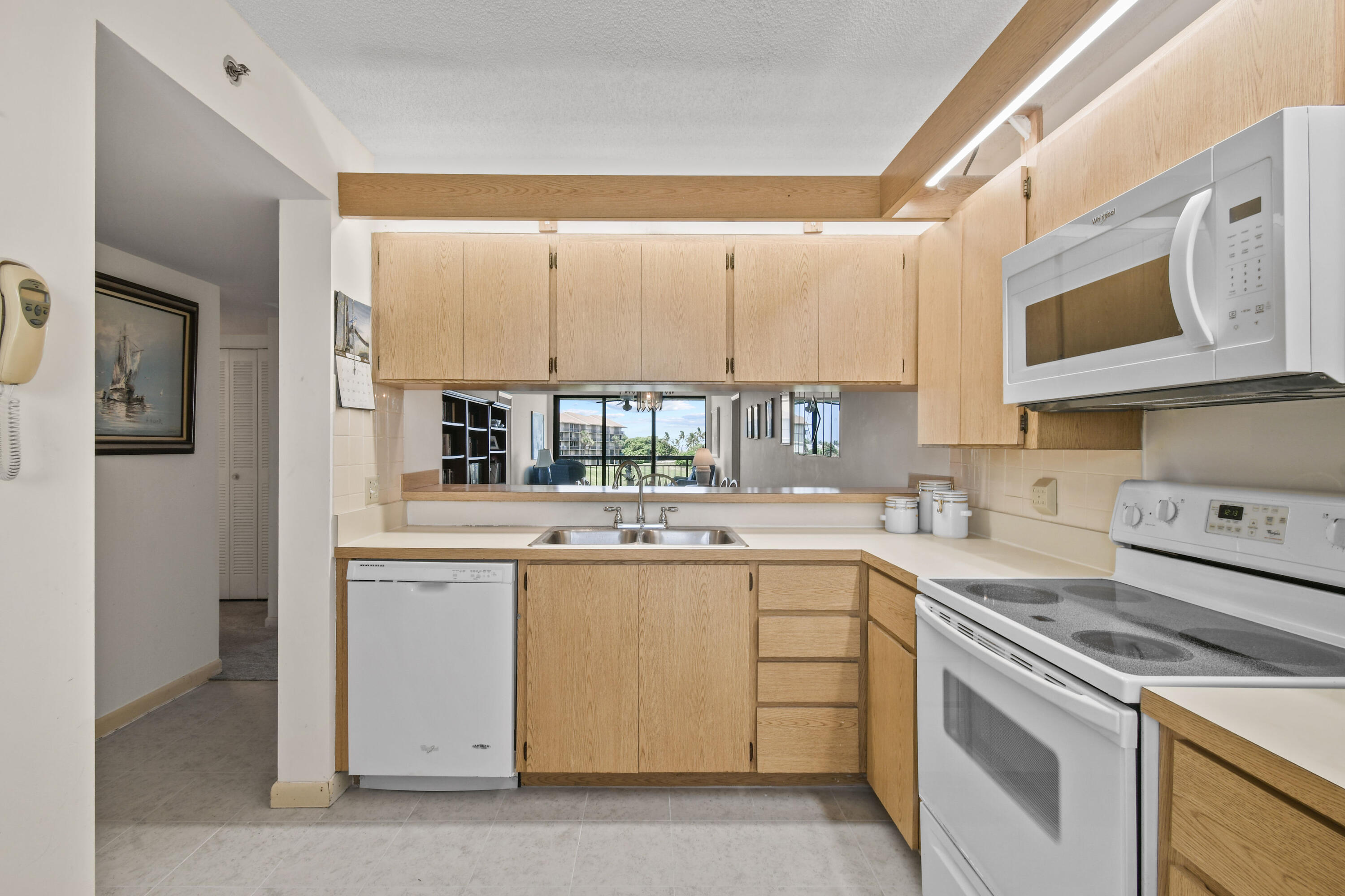 Condo kitchen with light wood cabinets, white appliances, and a pass-through overlooking the living area.