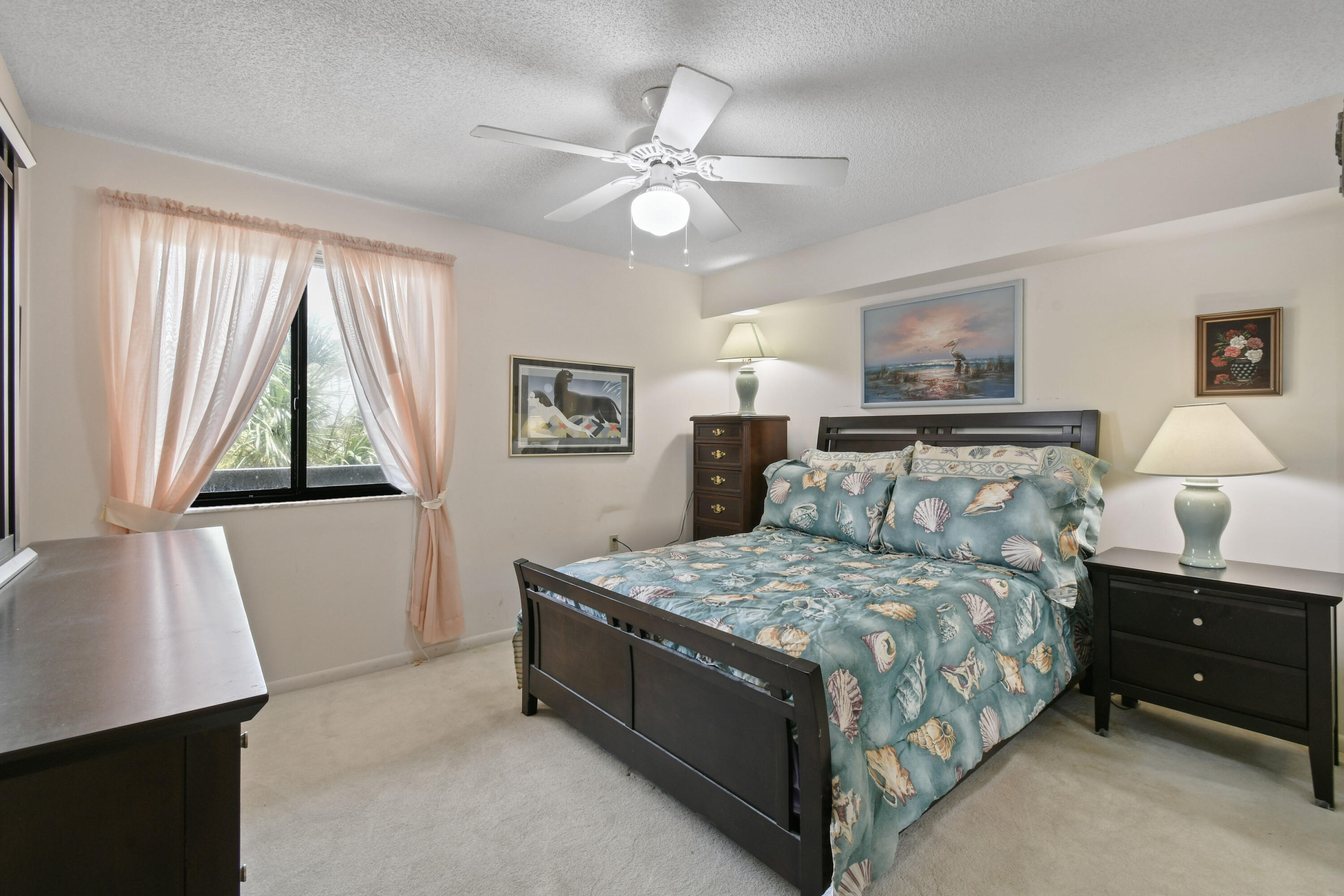 Bedroom with blue seashell-patterned bedding, dark wood furniture, and a curtained window.