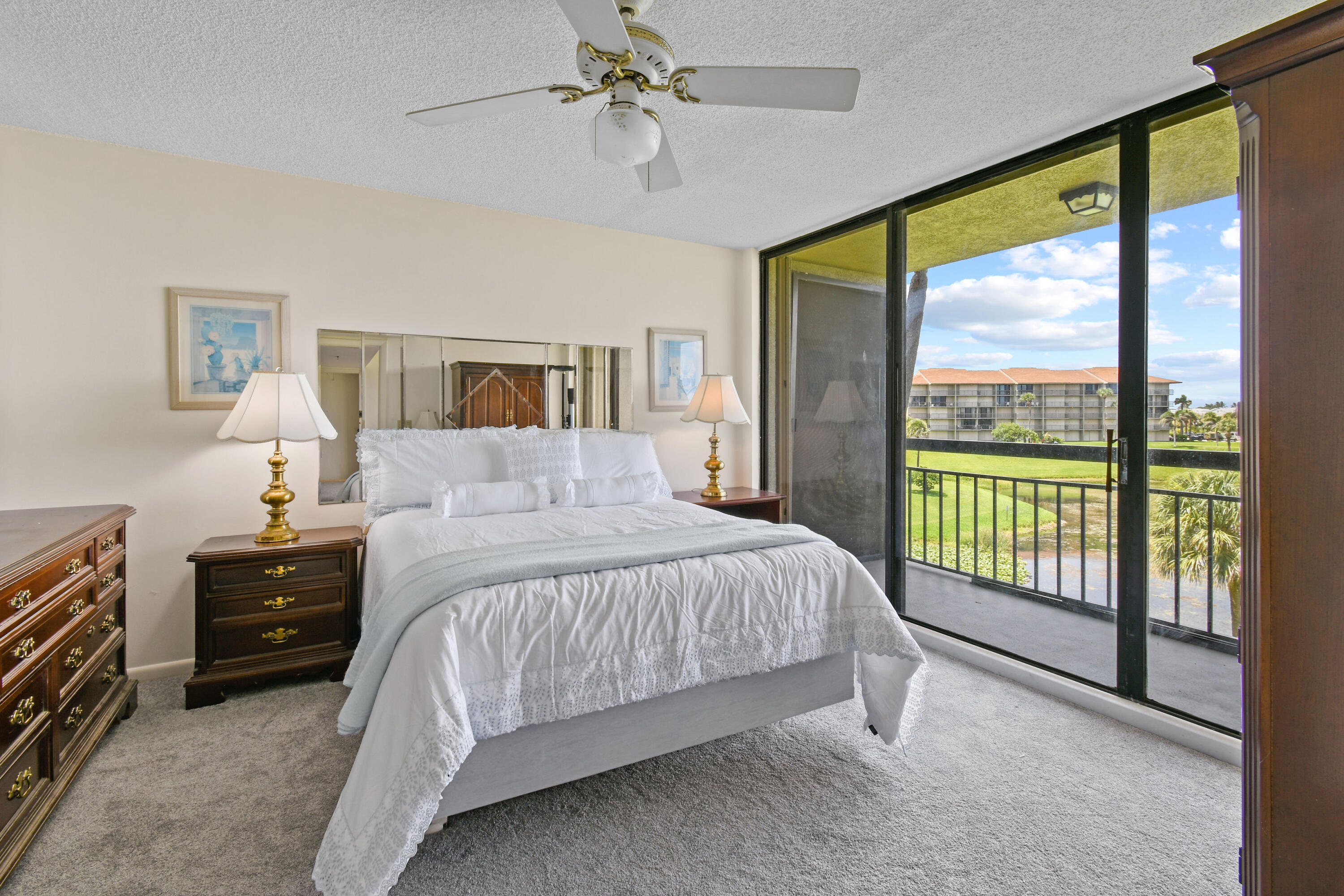 Bedroom with a white bed and sliding glass doors opening to a balcony overlooking a green lawn.