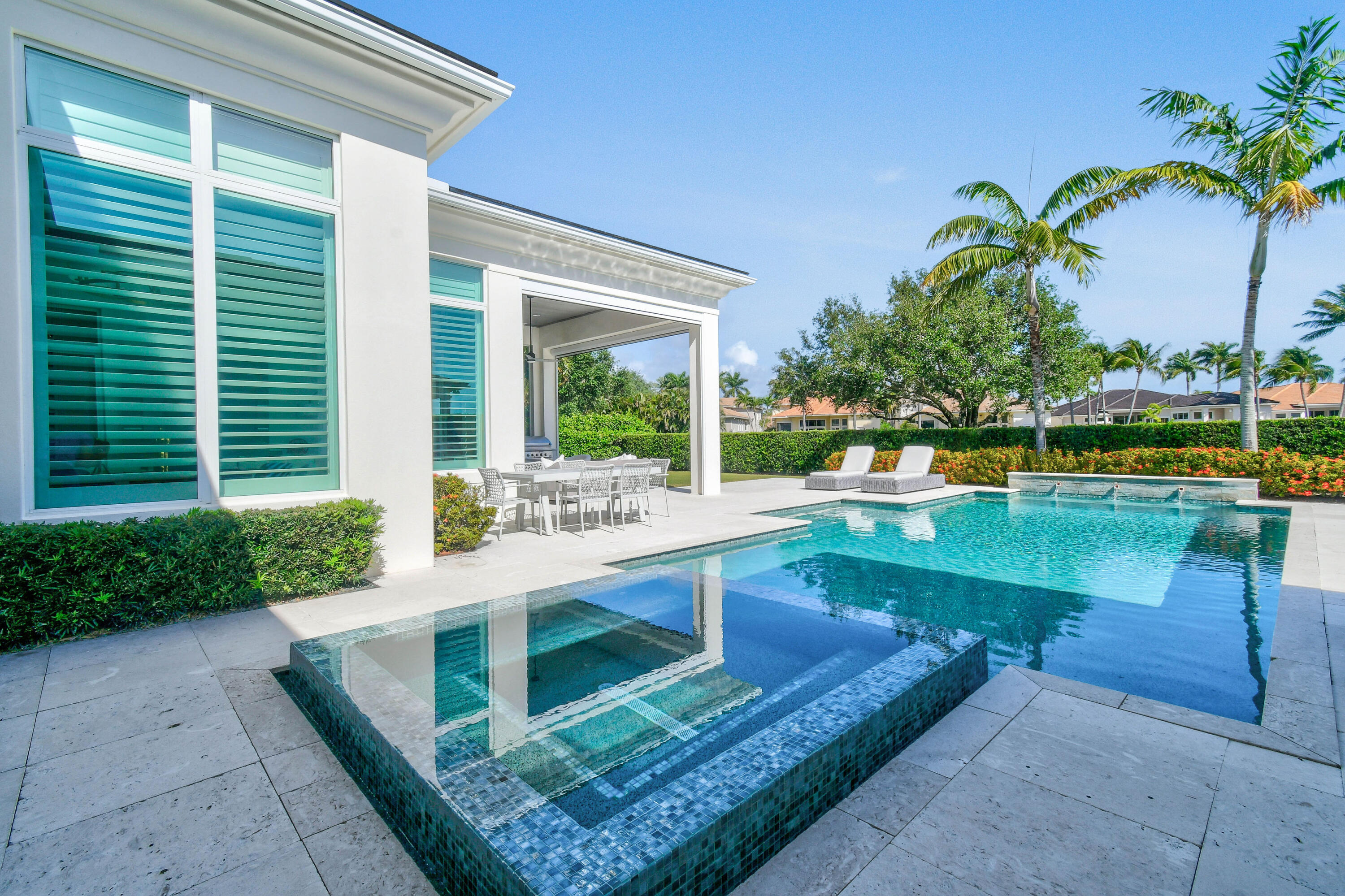 Modern home's backyard pool and raised tiled spa beside a covered patio with outdoor dining furniture.