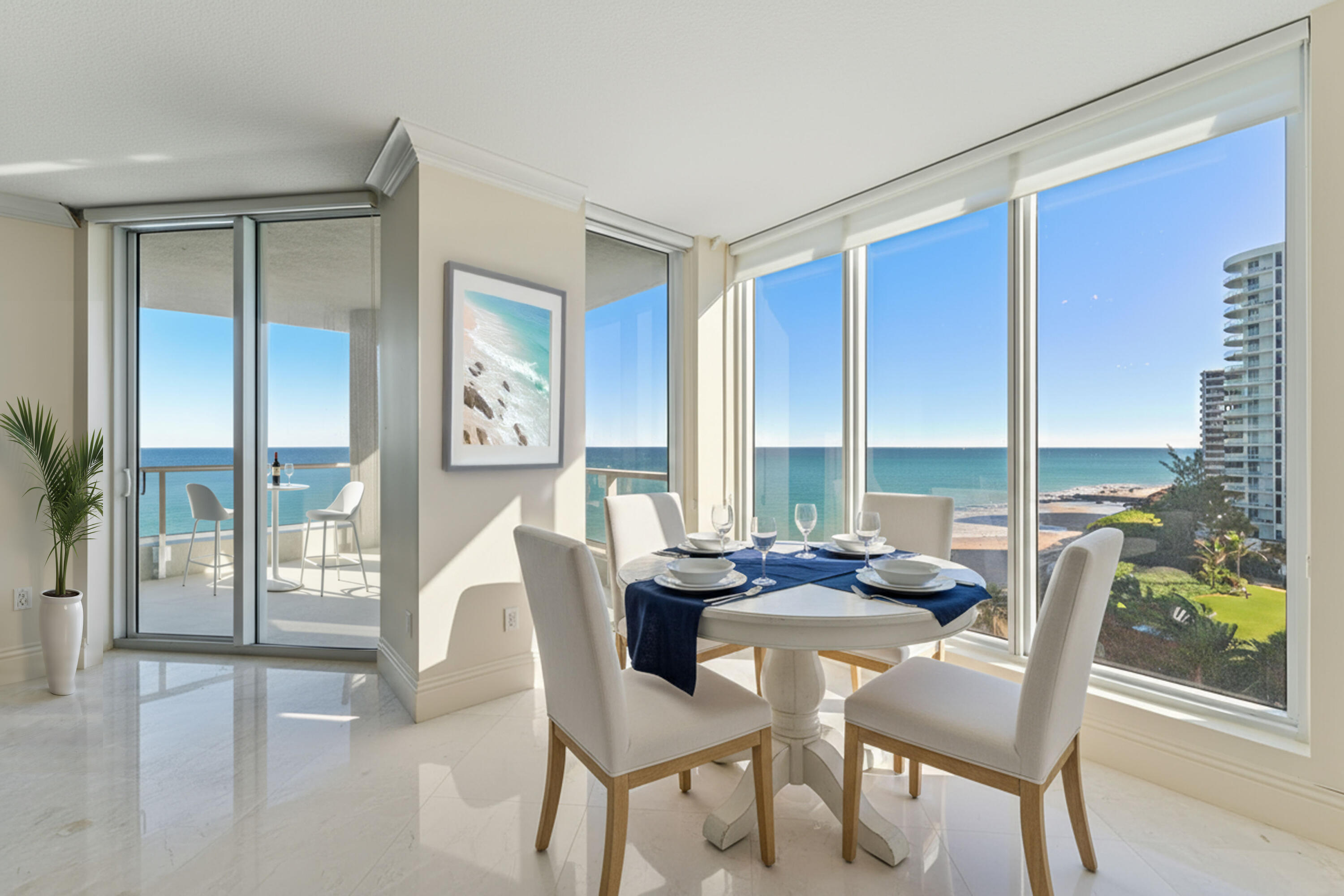 Dining area with a set table and floor-to-ceiling windows overlooking the ocean.