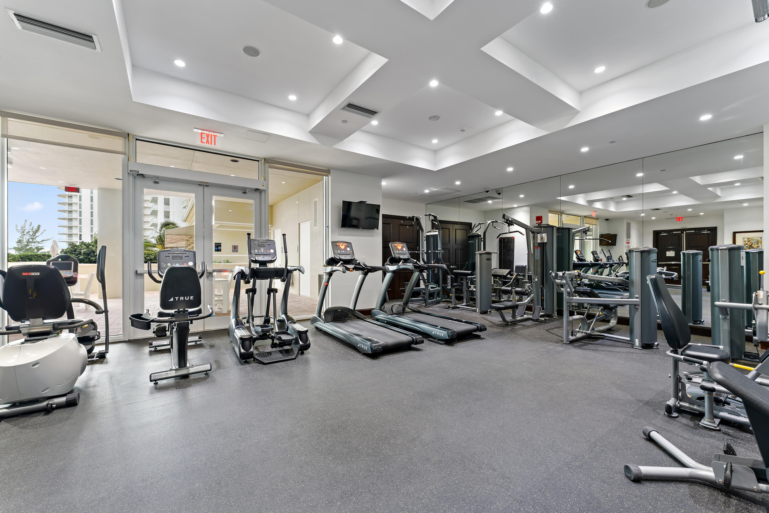 Condominium gym with rows of cardio and strength-training equipment beside large windows.