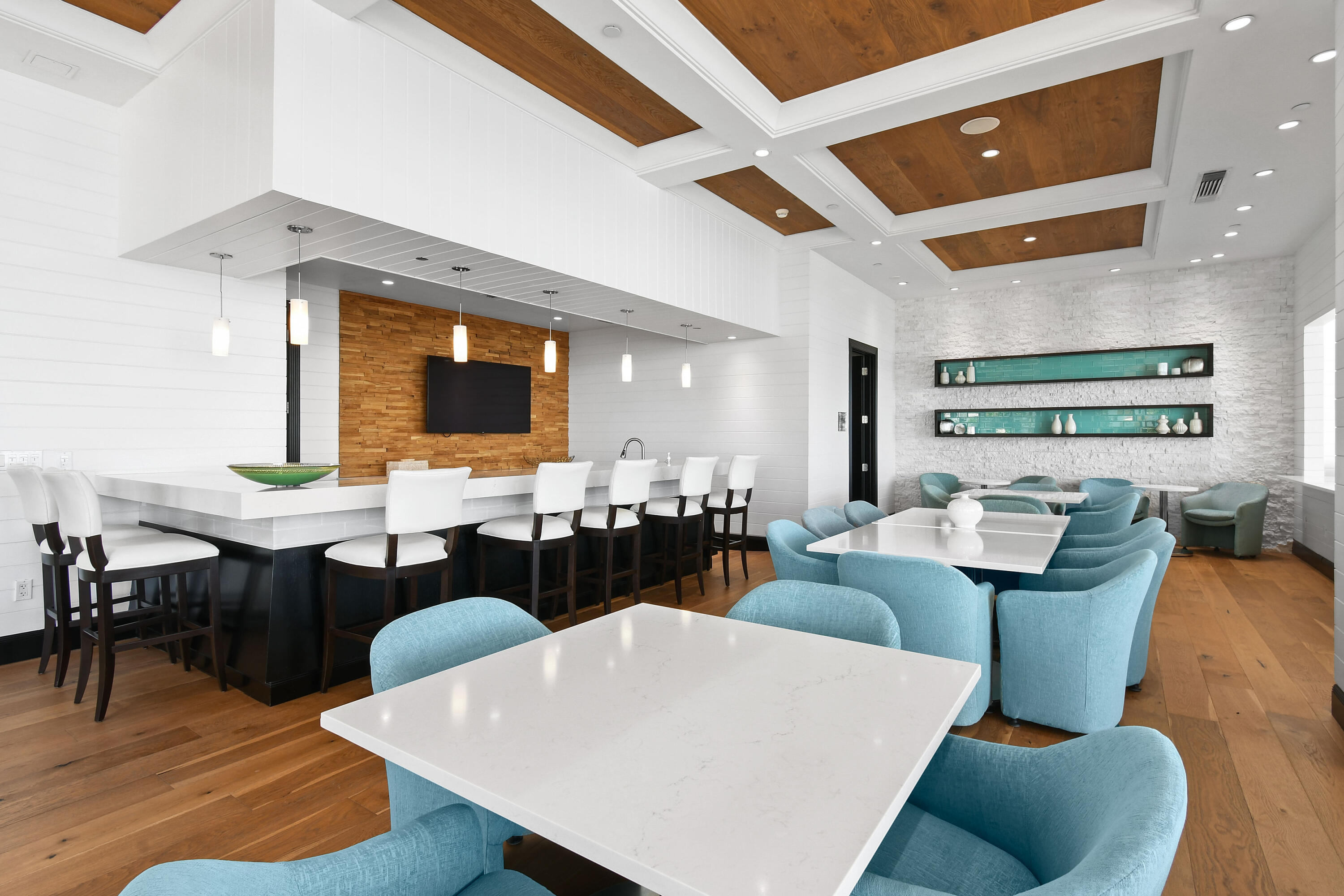 Furnished resident lounge with turquoise chairs, white tables, and a long bar counter.