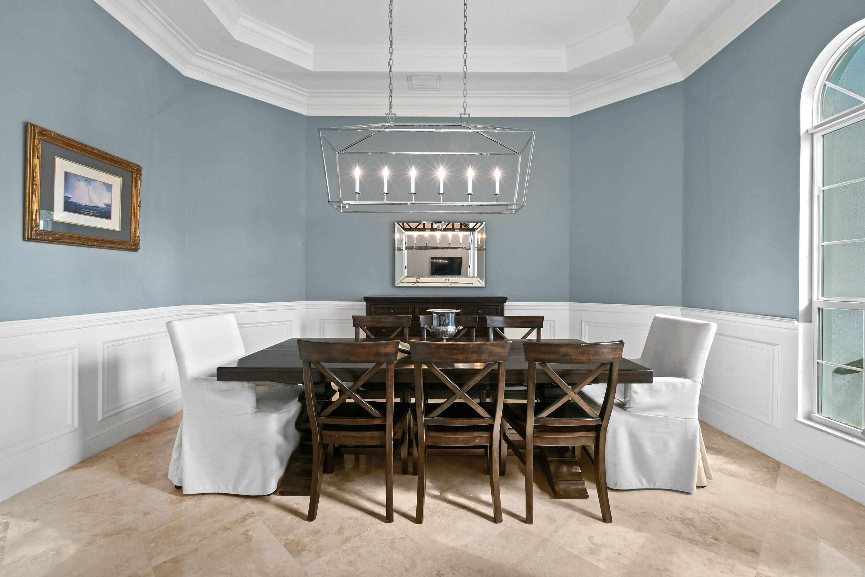 Dining room with a dark wood table, blue-gray walls, white wainscoting, and an arched window.