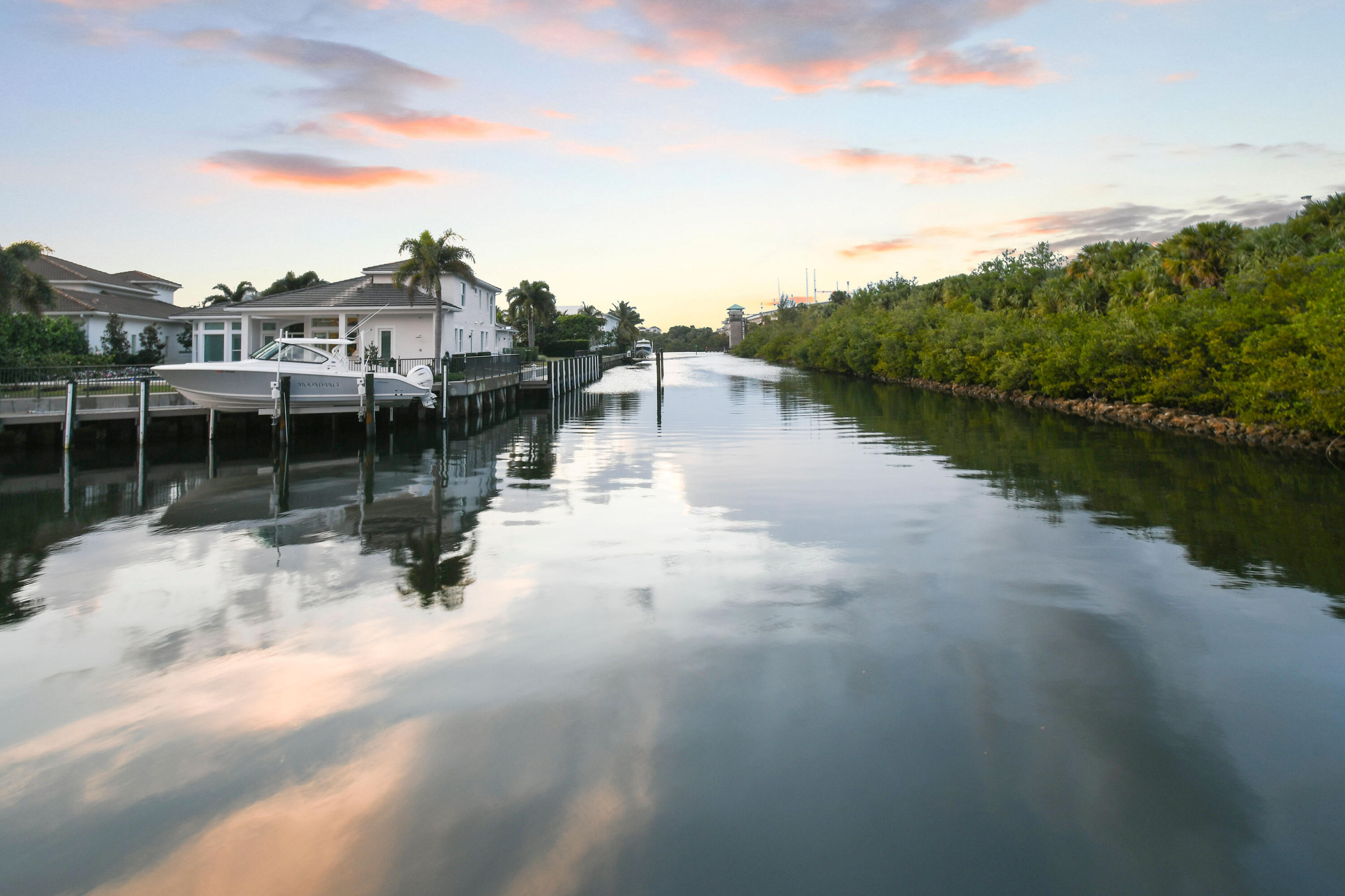 Residential canal at sunset with a docked white boat, waterfront homes, and mangroves.