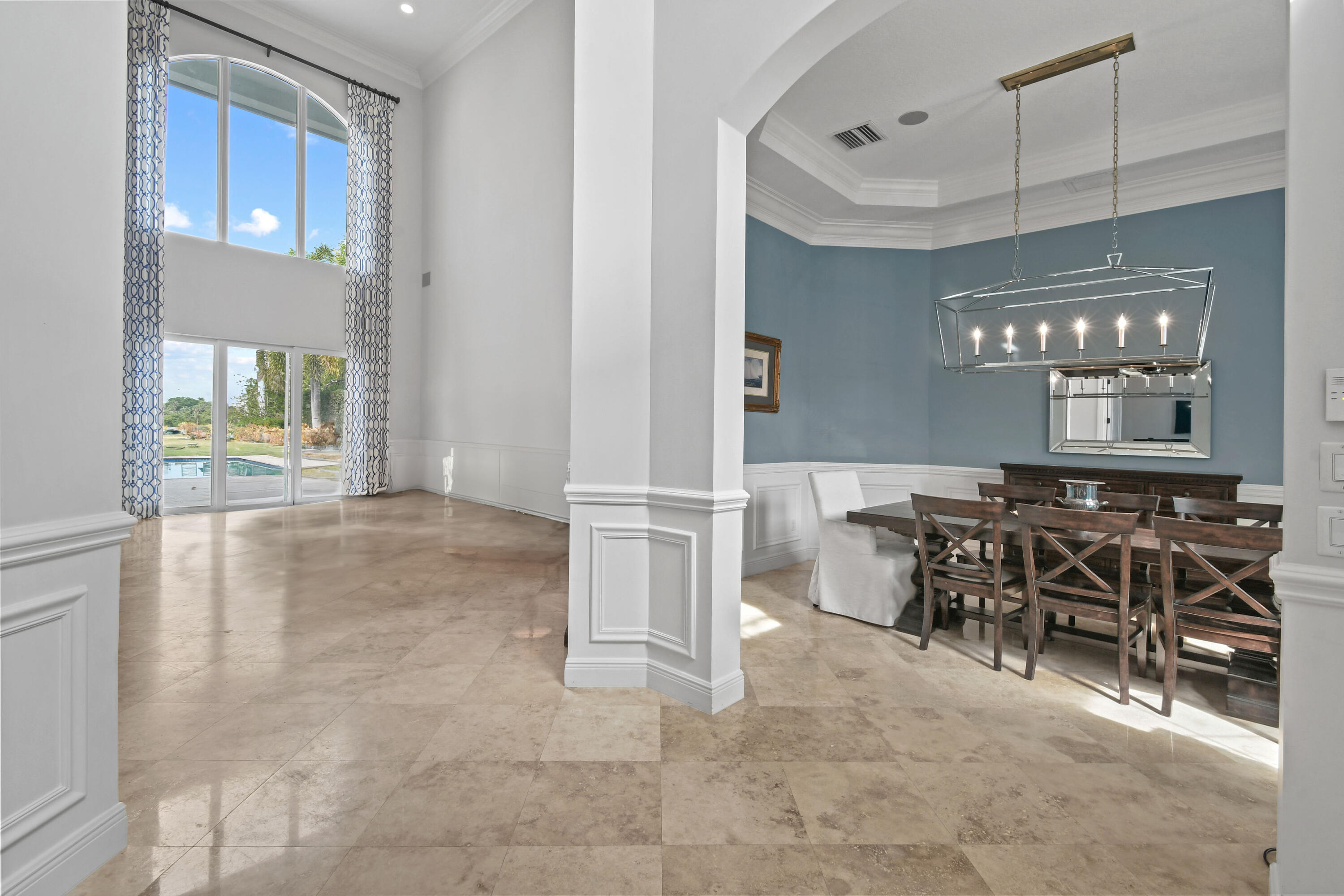 Dining room with a dark wood table, modern chandelier, and tall windows overlooking a pool.