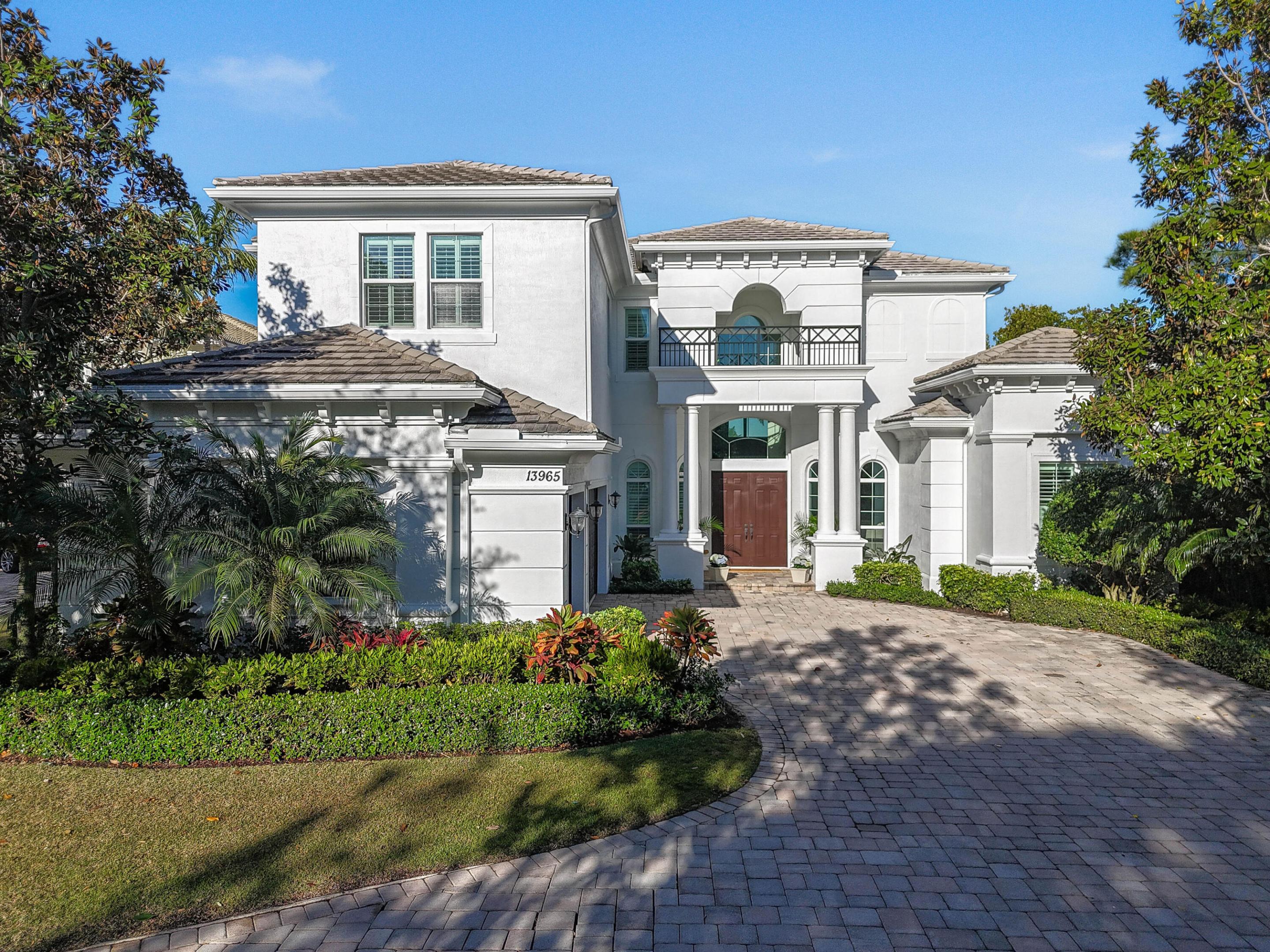White two-story house with a columned entrance, balcony, and curved paver driveway.