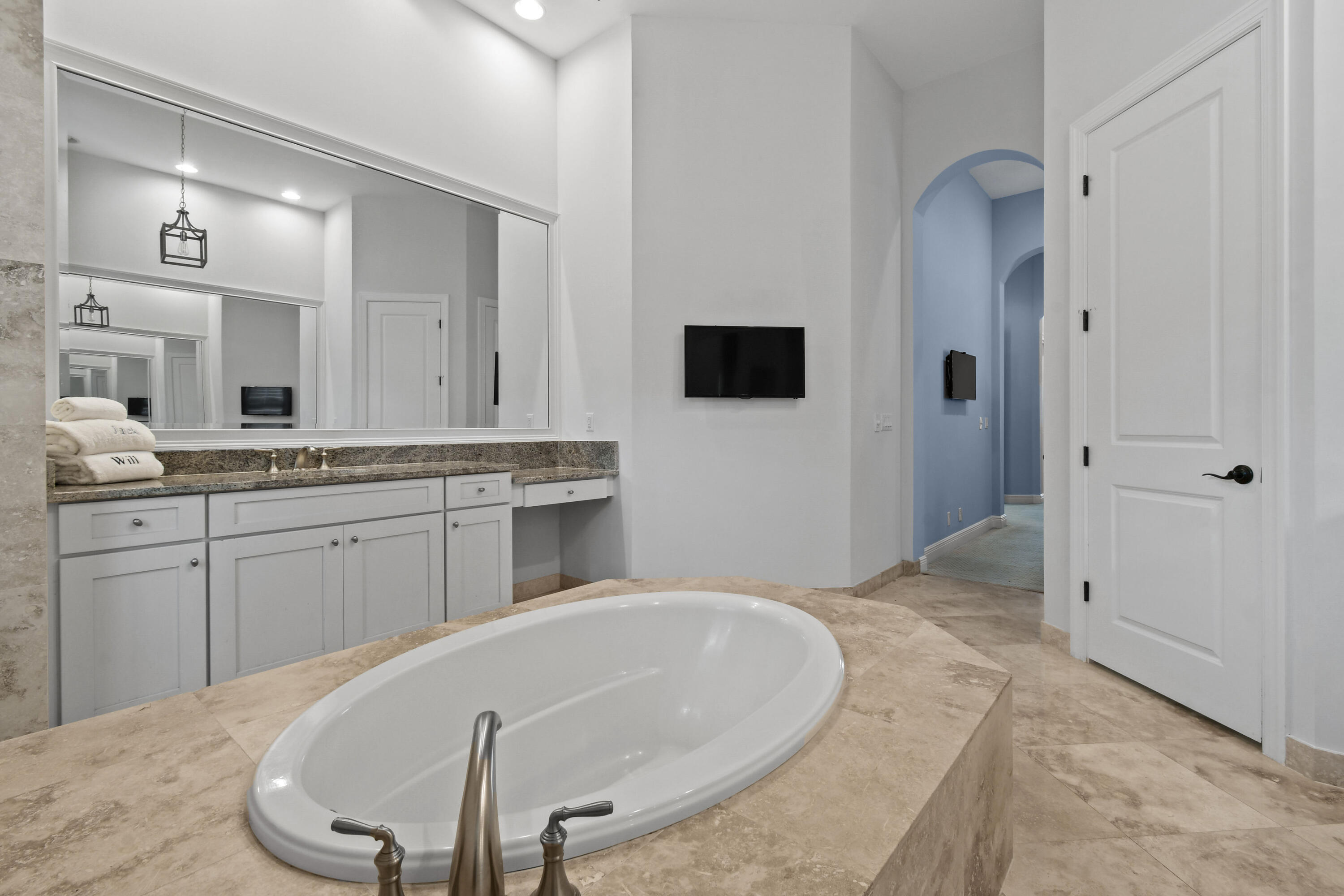 Primary bathroom with an oval soaking tub, granite vanity, and arched blue hallway.