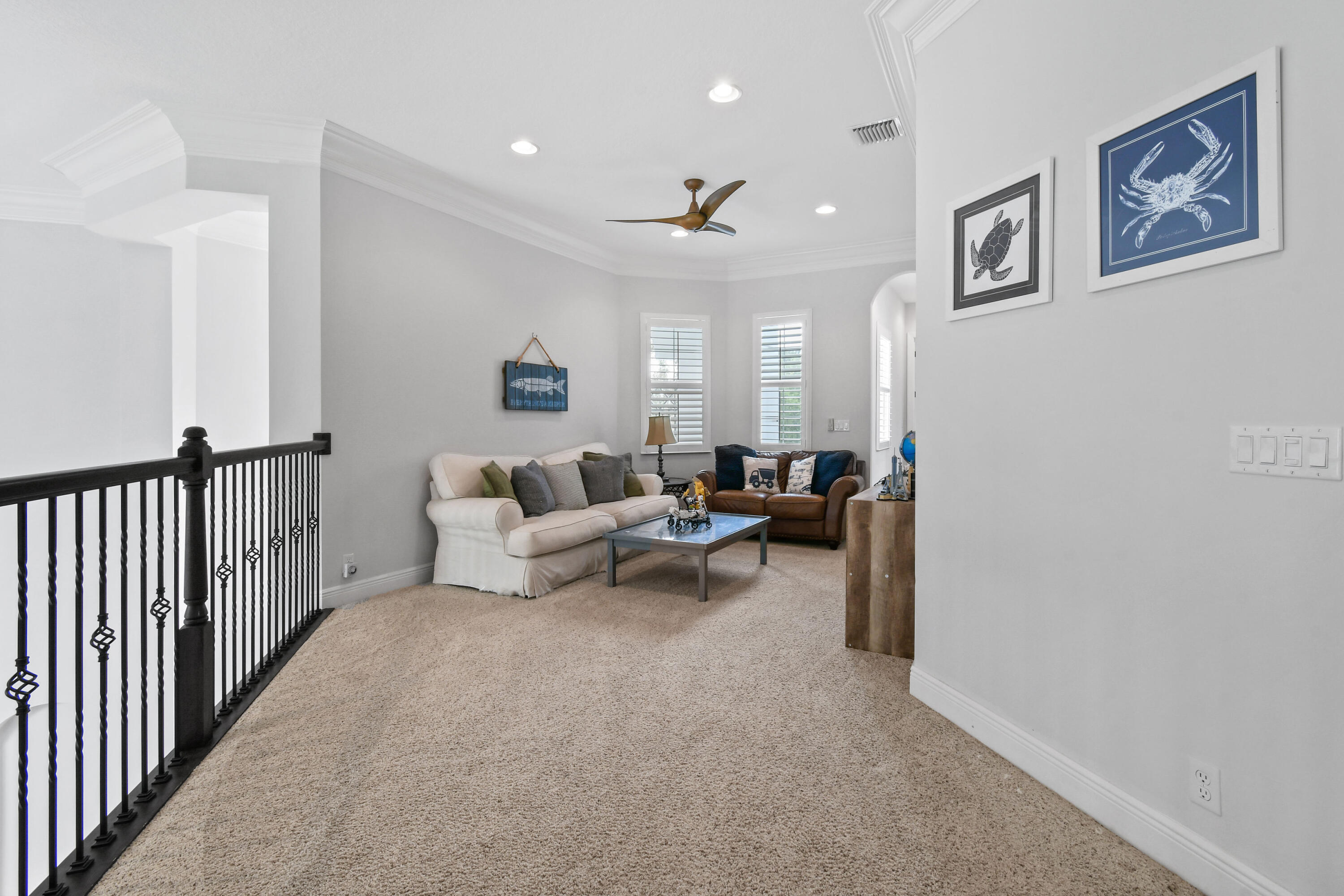 Upstairs sitting area with two sofas, shuttered windows, and framed coastal artwork beside a black stair railing.