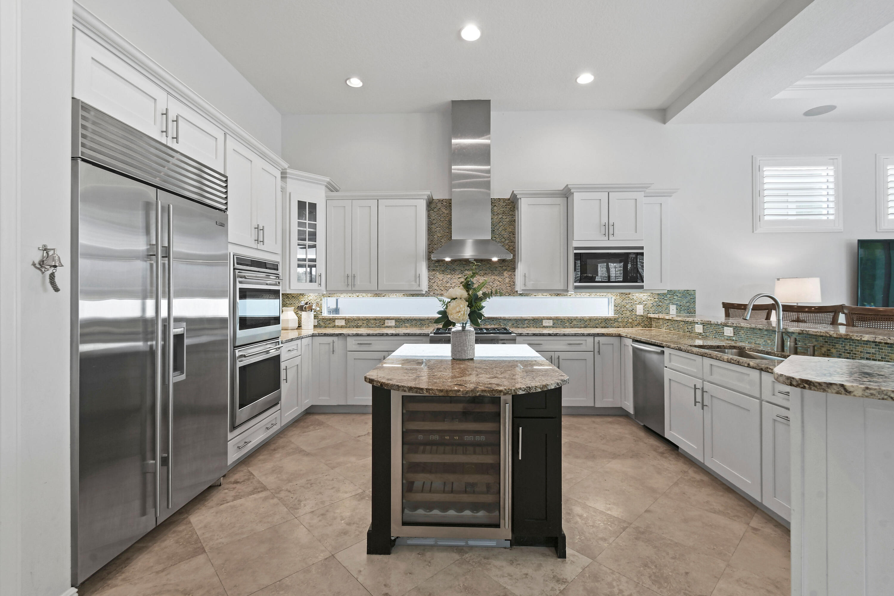 Kitchen with white cabinets, stainless steel appliances, mosaic backsplash, and a dark island with a wine refrigerator.