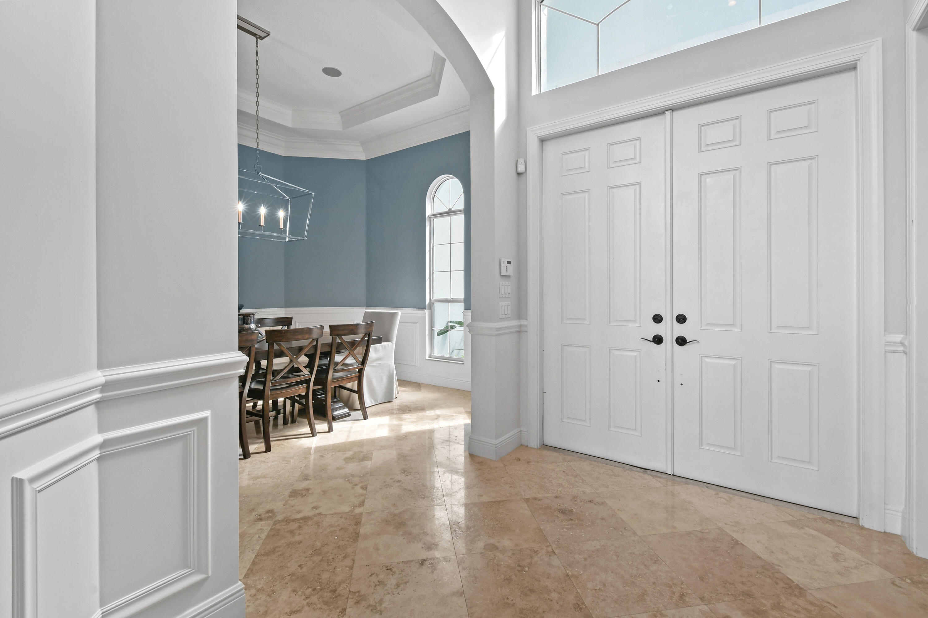 Entry foyer with paneled double doors, stone tile floors, and an adjoining dining area.