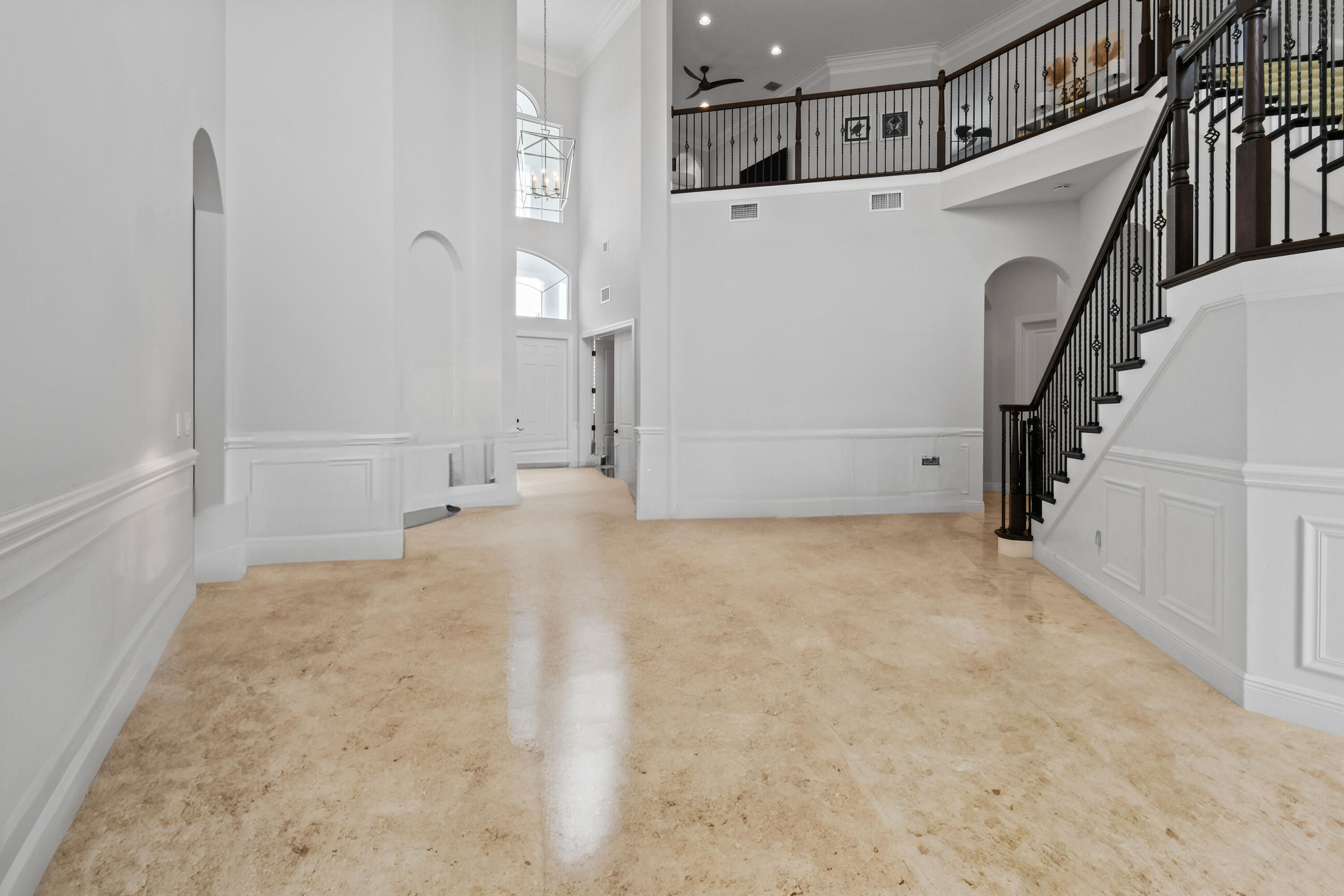 Two-story foyer with tan stone flooring, white paneled walls, and a dark-railed staircase.