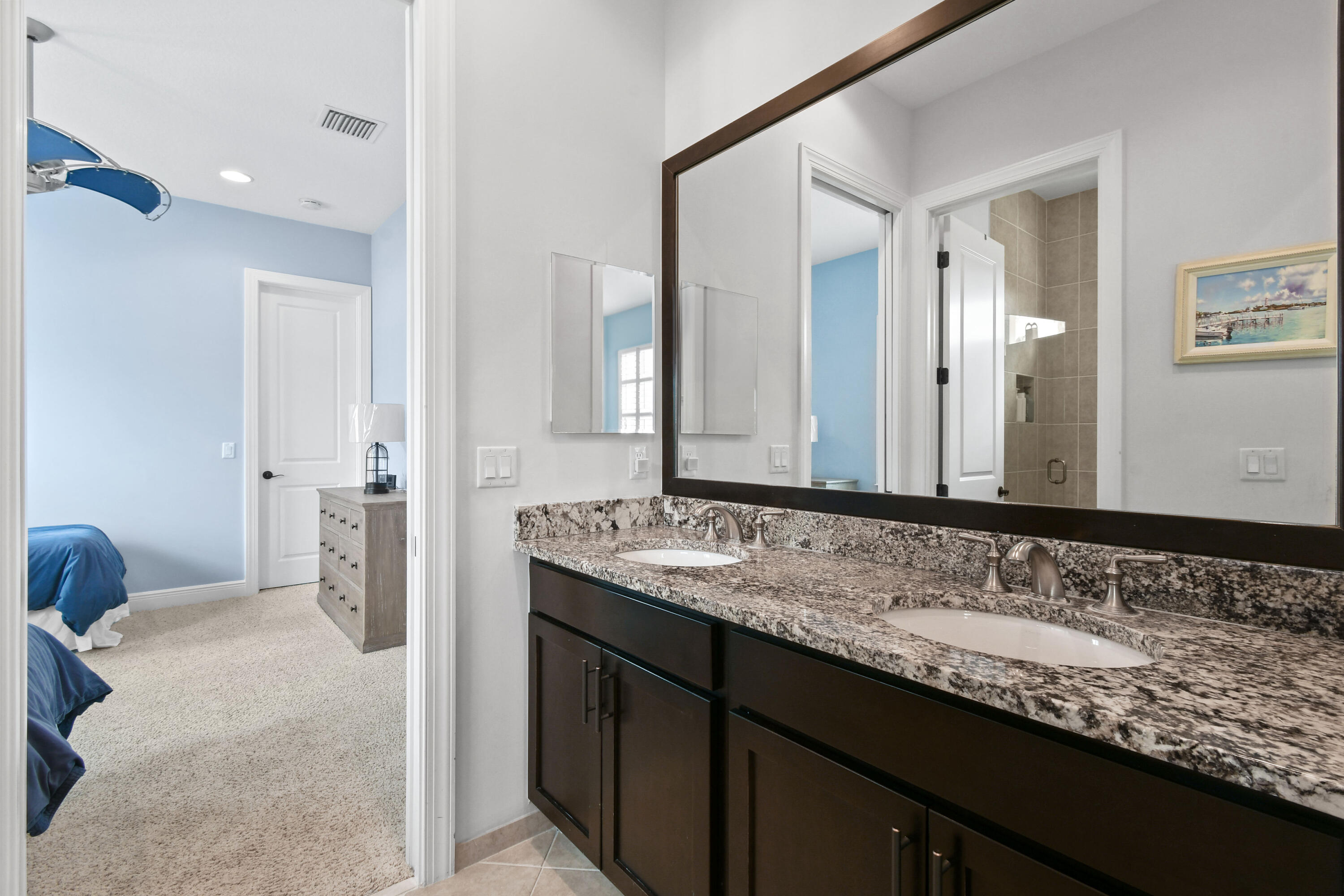 Bathroom with double-sink granite vanity and a view into a blue bedroom.
