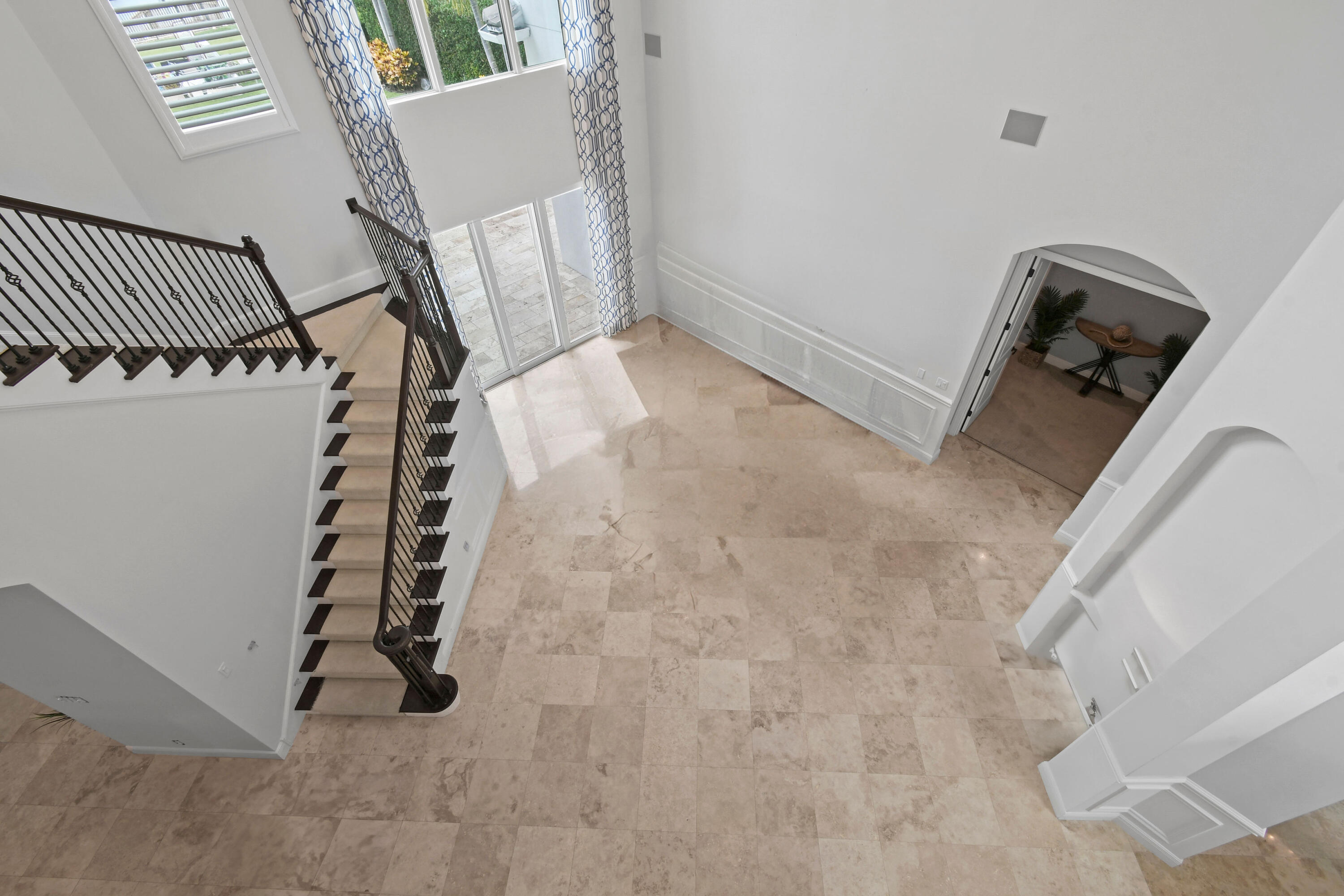 Double-height foyer with beige stone tile, dark-railed staircase, and tall windows.