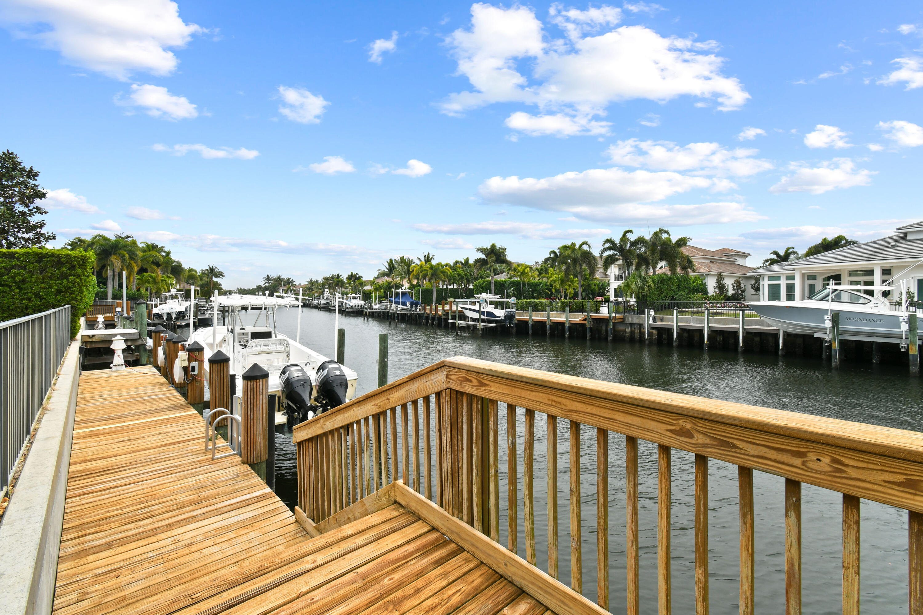 Wooden dock overlooks a palm-lined residential canal with boats and waterfront homes.