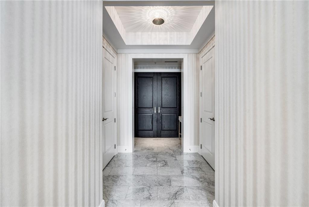 Apartment entry hallway with marble floors, white doors, and dark double doors at the far end.