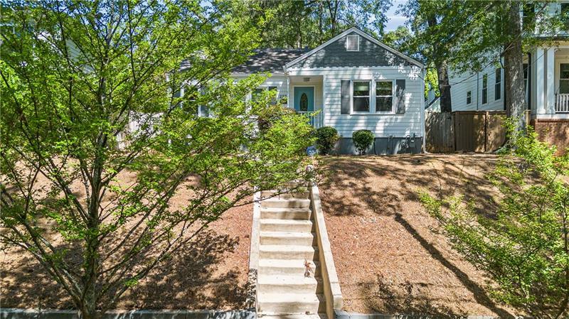 Light blue-gray house with white trim, front steps, and a sloped, tree-shaded yard.