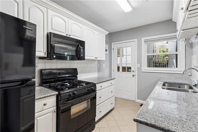 Kitchen with white cabinets, black appliances, granite counters, and a sink beneath the window.