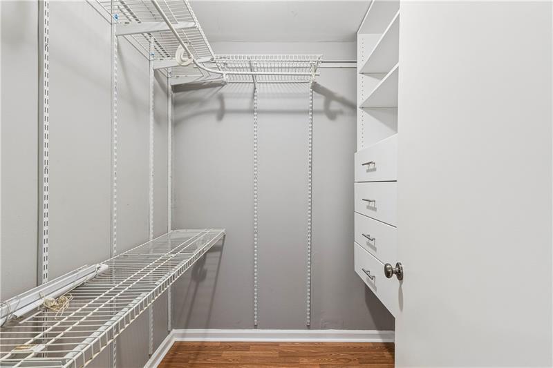 Walk-in closet with white wire shelving, hanging racks, built-in drawers, and hardwood flooring.