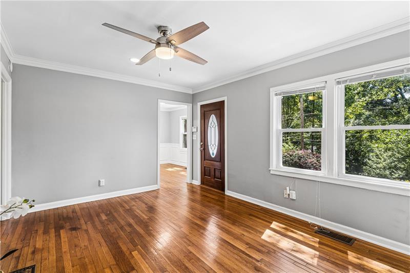 Empty room with polished hardwood floors, gray walls, a ceiling fan, and large windows.