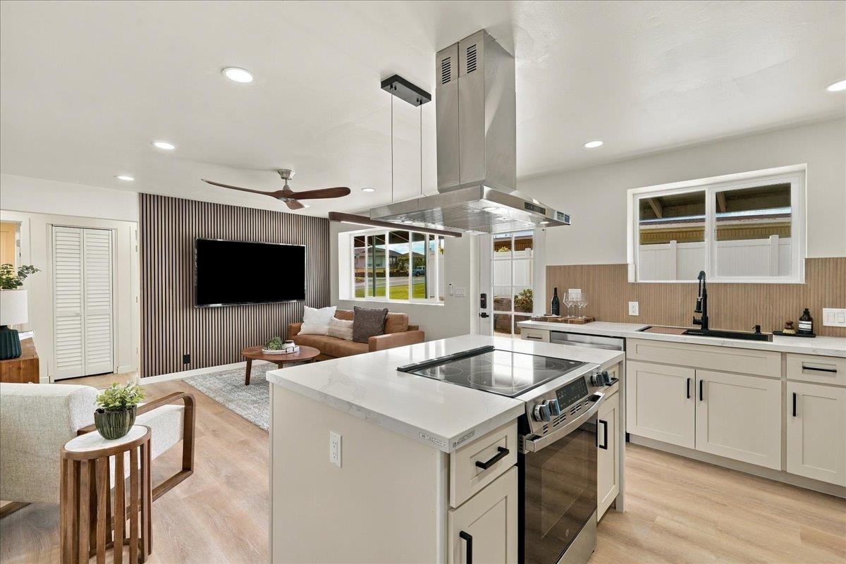 Modern open-plan kitchen with a large cooktop island, stainless hood, and furnished living area.