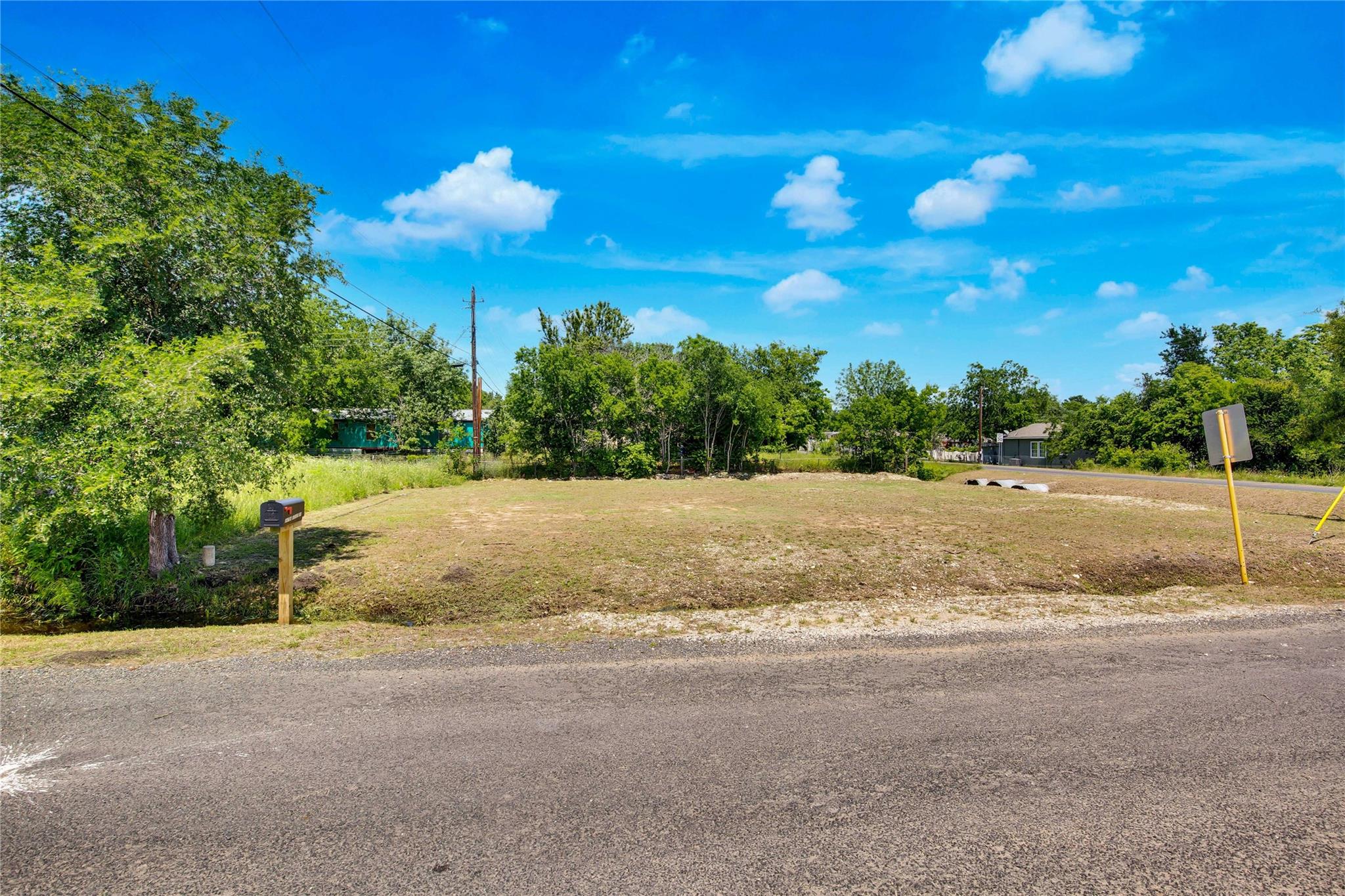 Vacant roadside lot with cleared ground, trees along the edges, and a mailbox at the street.