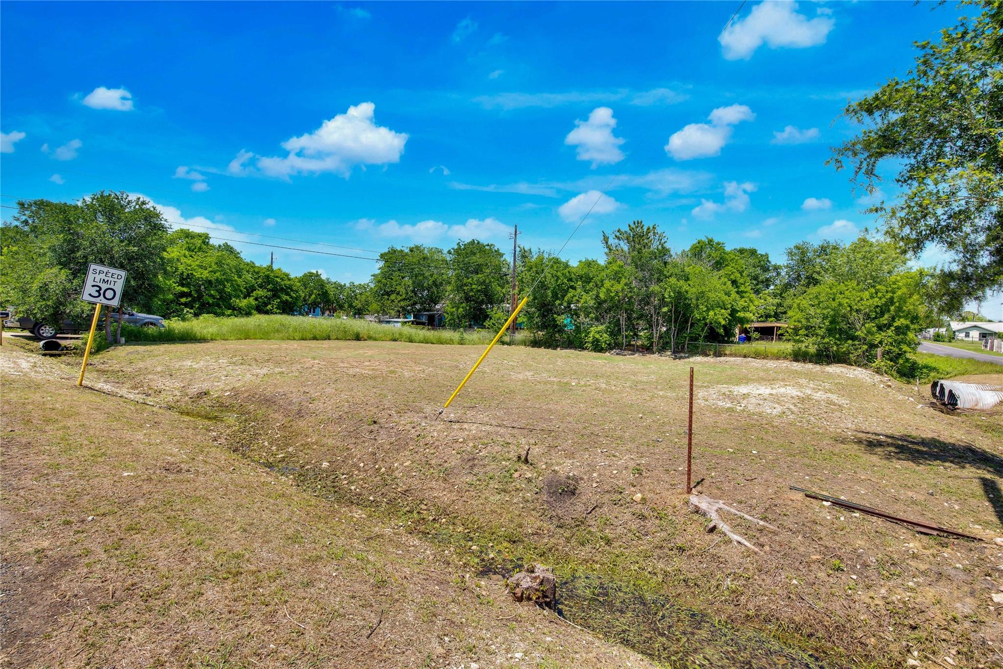 Cleared vacant lot with patchy ground, utility markers, and trees along the rear boundary.