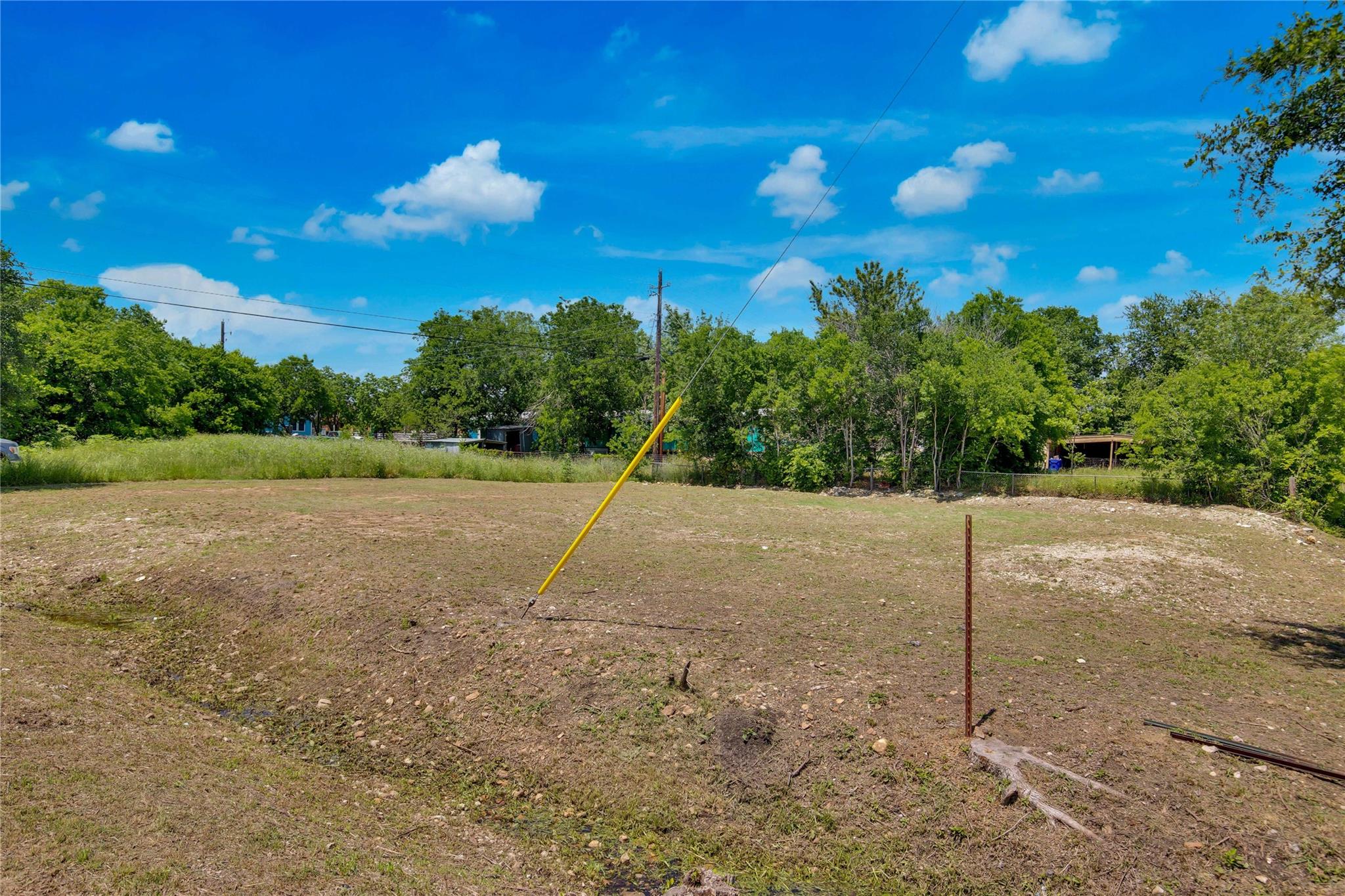 Cleared residential lot with dry ground, utility lines, and trees along the back edge.