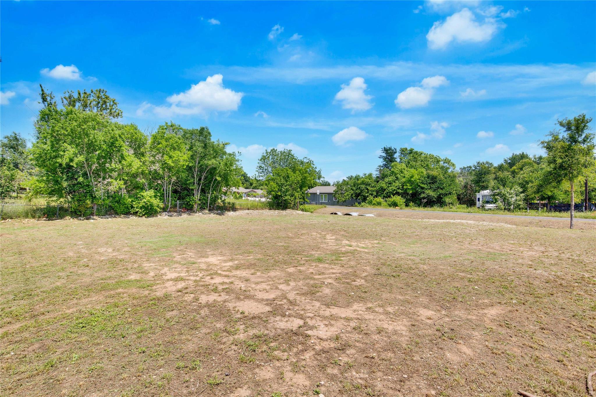 Cleared grassy lot bordered by trees, with neighboring homes in the distance.