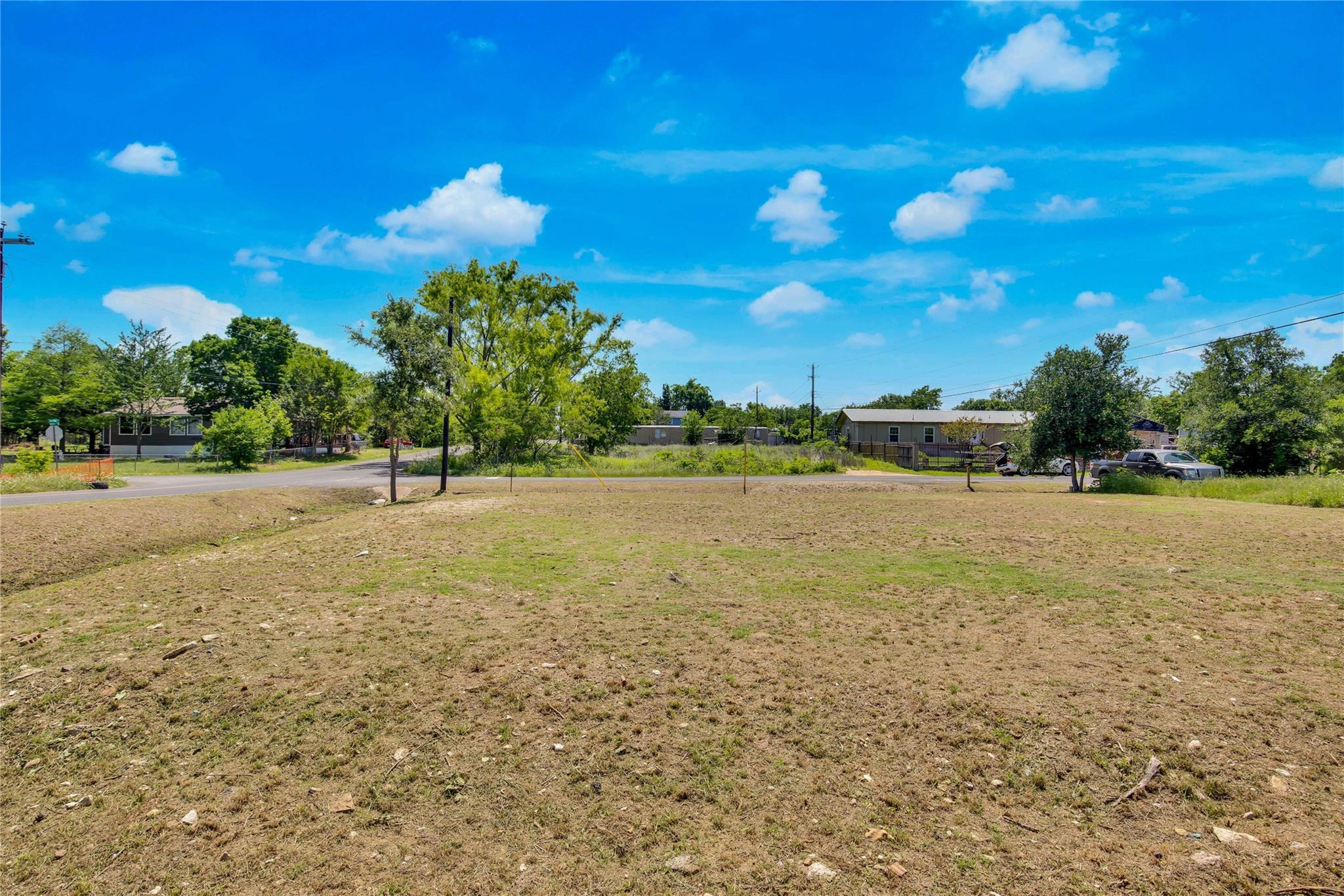 Vacant lot with dry grass and scattered trees, neighboring homes across the street.