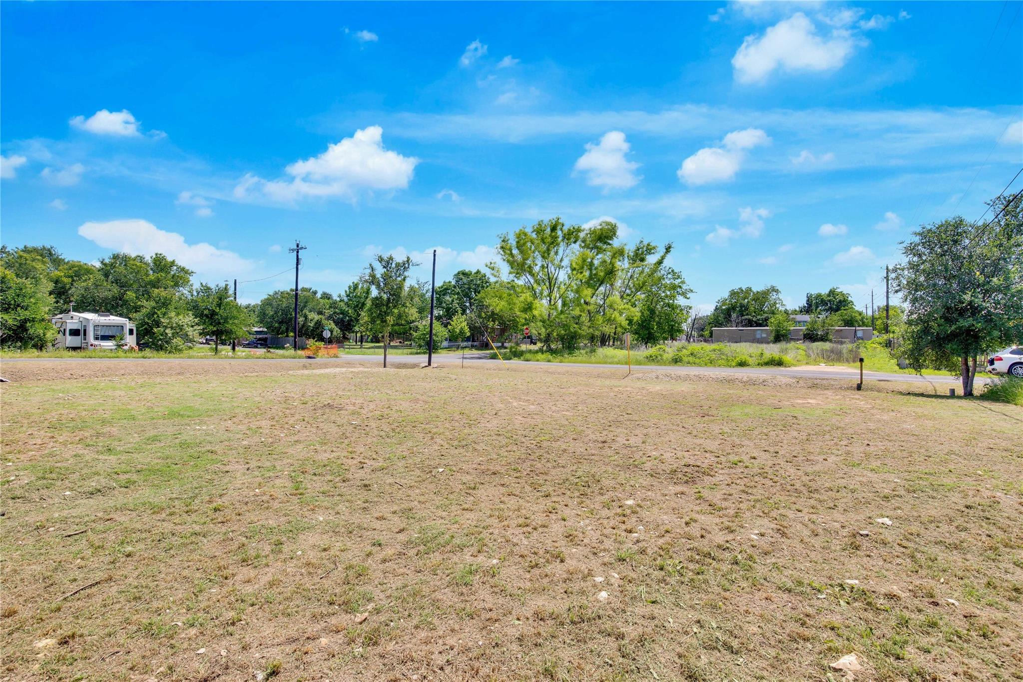 Open grassy lot with a road and trees along its far edge.