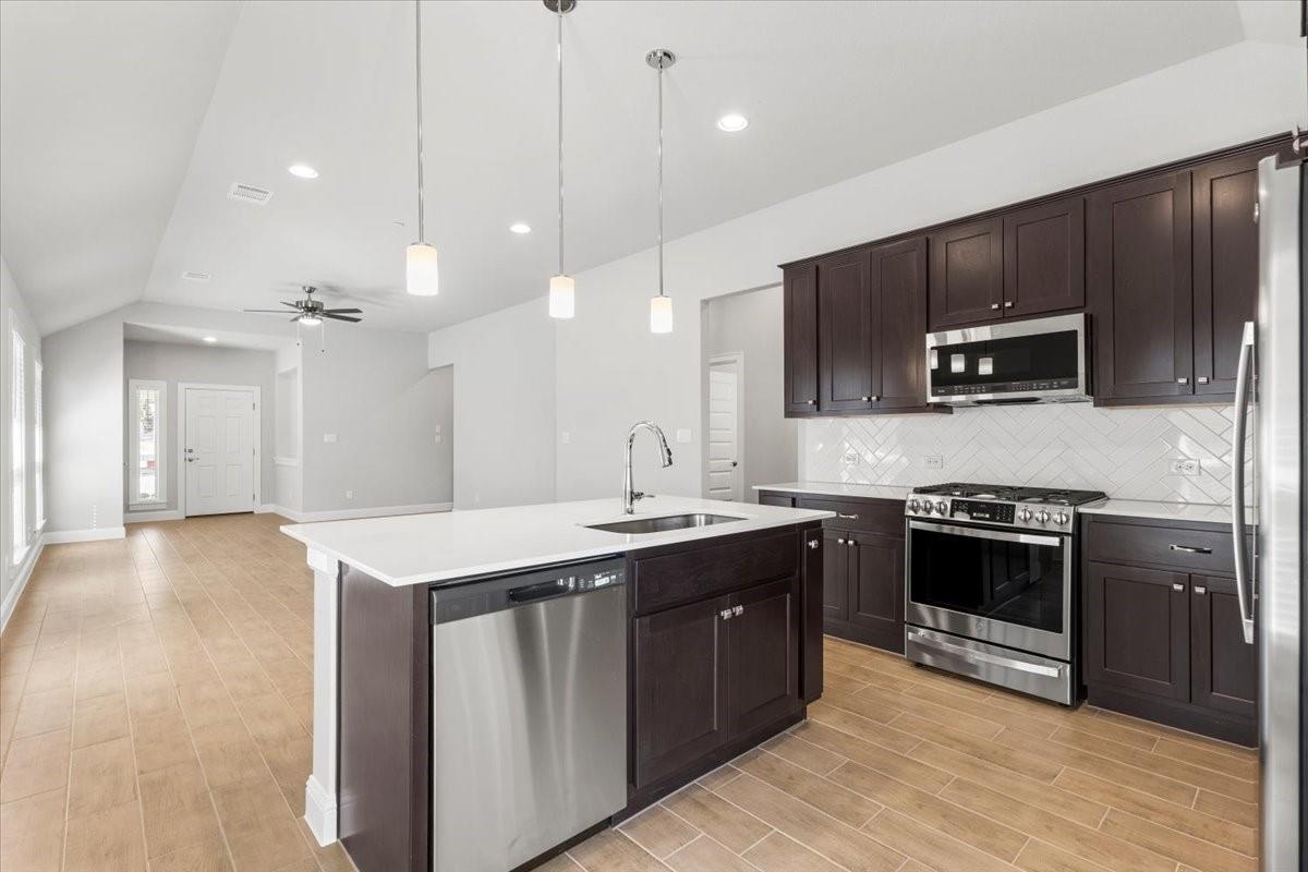 Kitchen with dark wood cabinets, stainless steel appliances, and a large island beneath pendant lights.