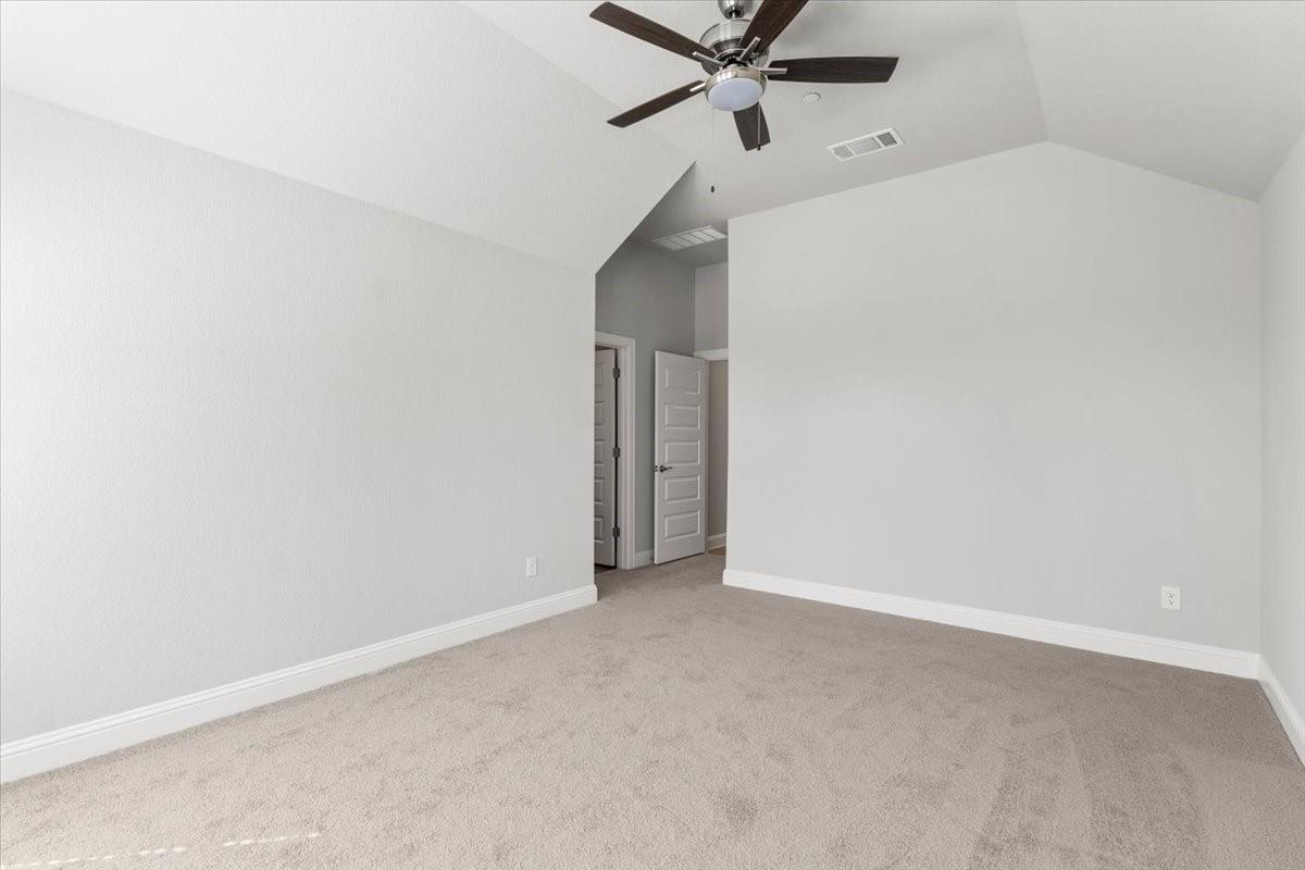 Empty carpeted bedroom with a vaulted ceiling and dark ceiling fan.