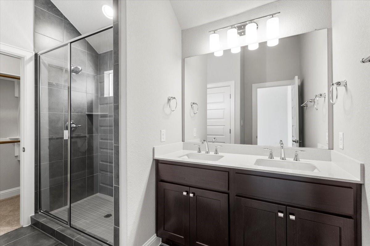 Bathroom with a dark double vanity and glass-enclosed gray-tile shower.