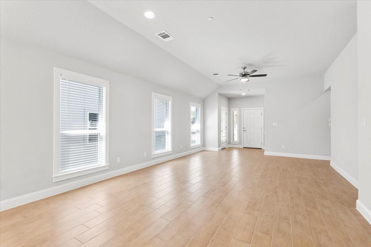 Vacant living room with light wood-look flooring, three tall windows, and a ceiling fan.
