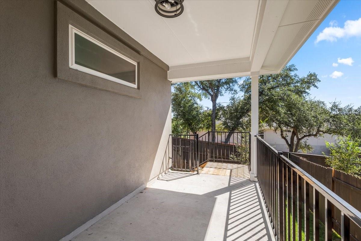Covered balcony with dark metal railings overlooking trees and a fenced yard.