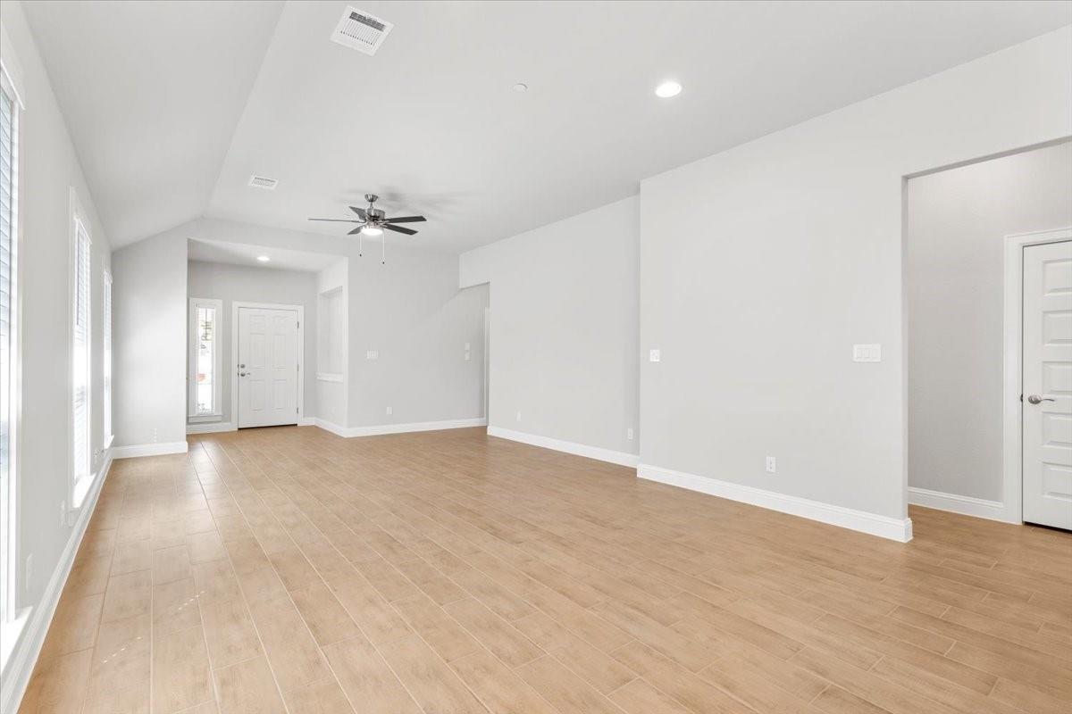 Empty living room with wood-look tile flooring, tall windows, and a ceiling fan.