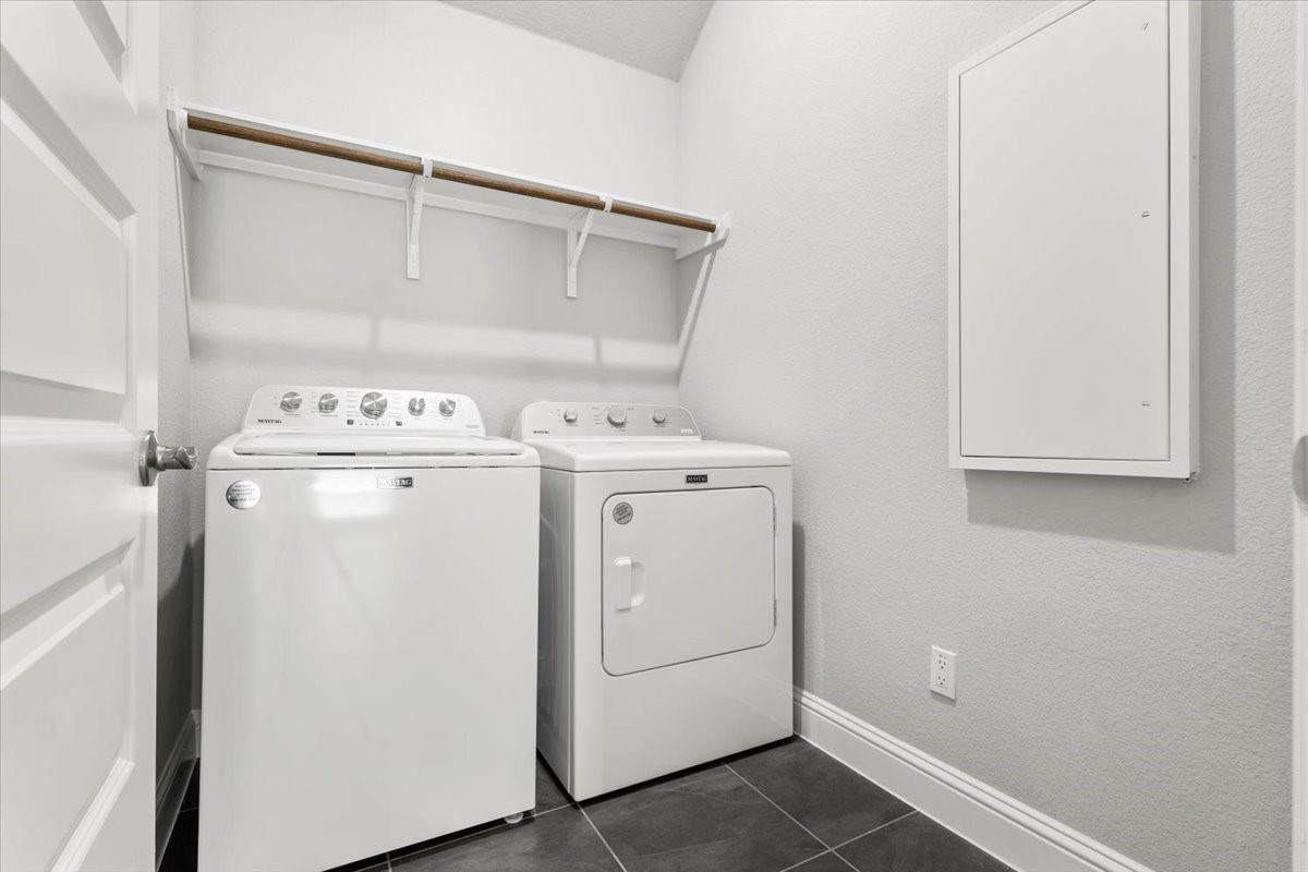 Laundry room with a white washer and dryer beneath a wall-mounted shelf.