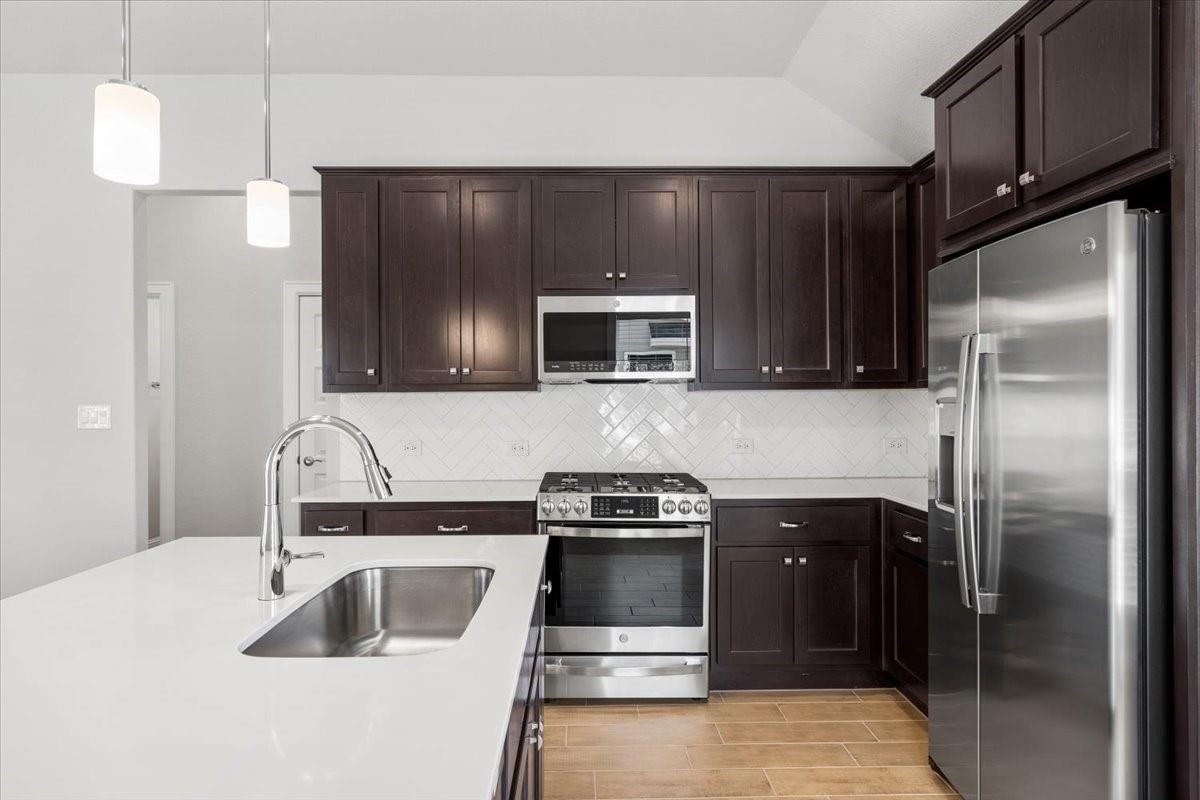 Modern kitchen with dark cabinets, stainless appliances, and a white island with an undermount sink.