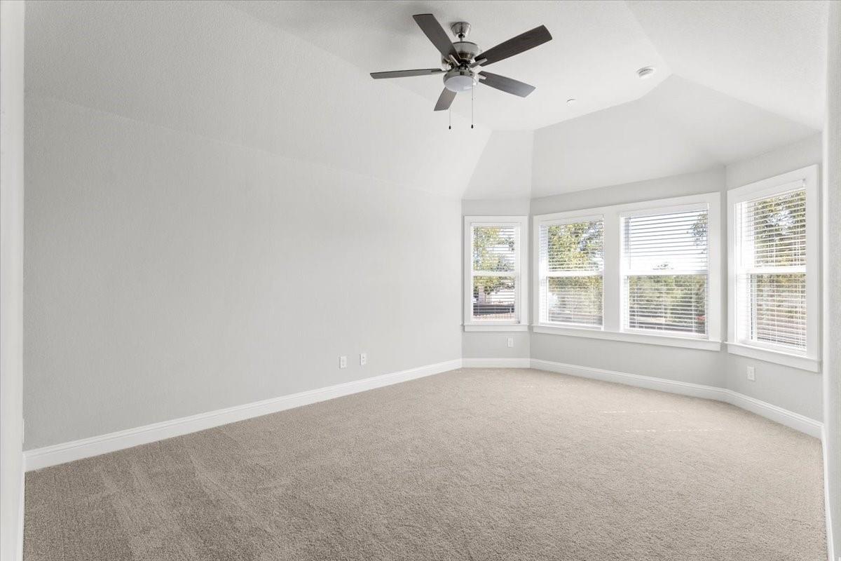 Empty bedroom with beige carpet, ceiling fan, and multiple windows with blinds.
