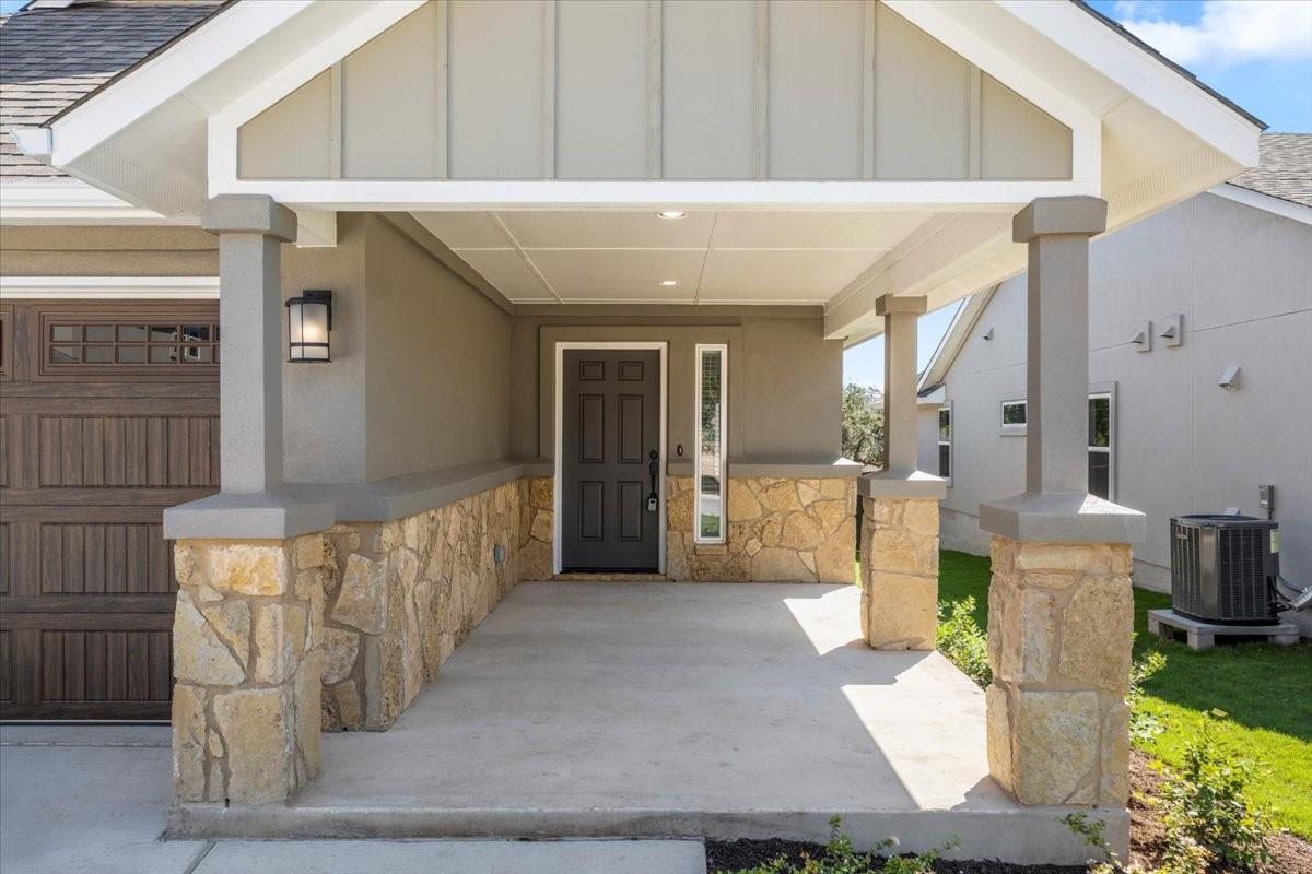 Covered home entrance with stone columns, a dark front door, and a wood garage door.