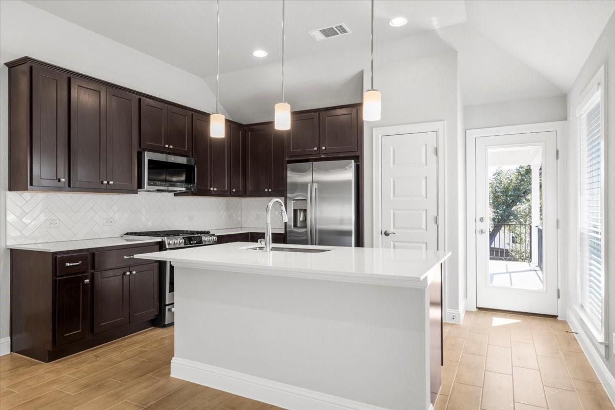 Kitchen with dark wood cabinets, a white island, stainless steel appliances, and a glass door to the balcony.